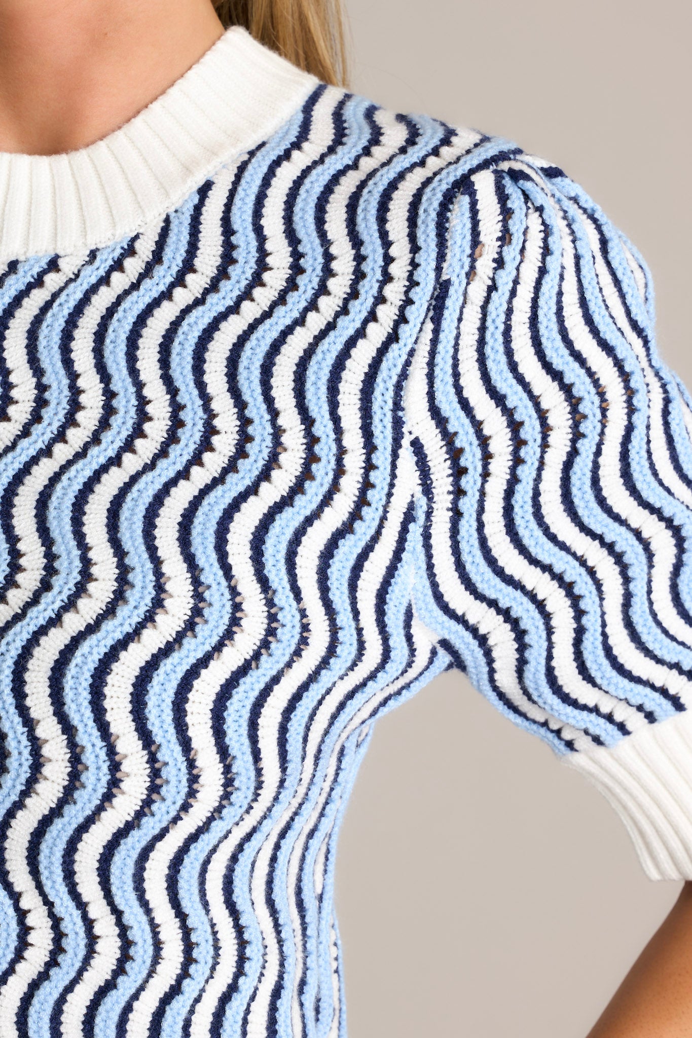 Close-up of the blue stripe sweater top showing the high knit neckline, the texture of the soft knit fabric, and the wavy blue and white stripe design.