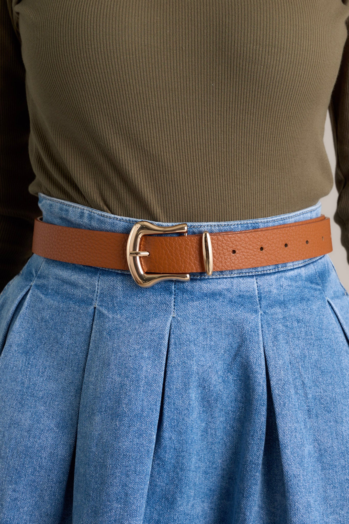 Close-up of this brown belt that features a gold rounded square shape buckle, a gold point at the end of the belt and a brown textured belt.