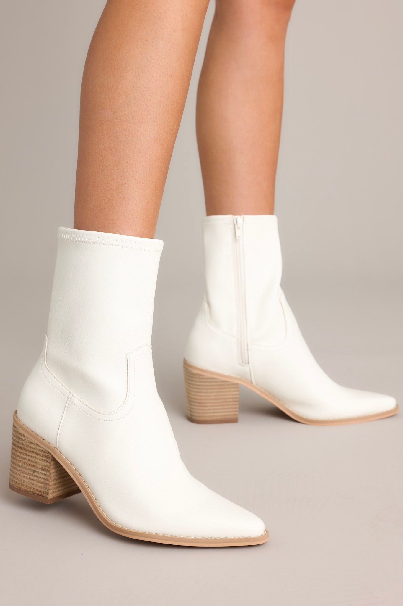 Side view of these white boots that feature a pointed toe, a platform heel, a discrete side zipper and a tan sole.