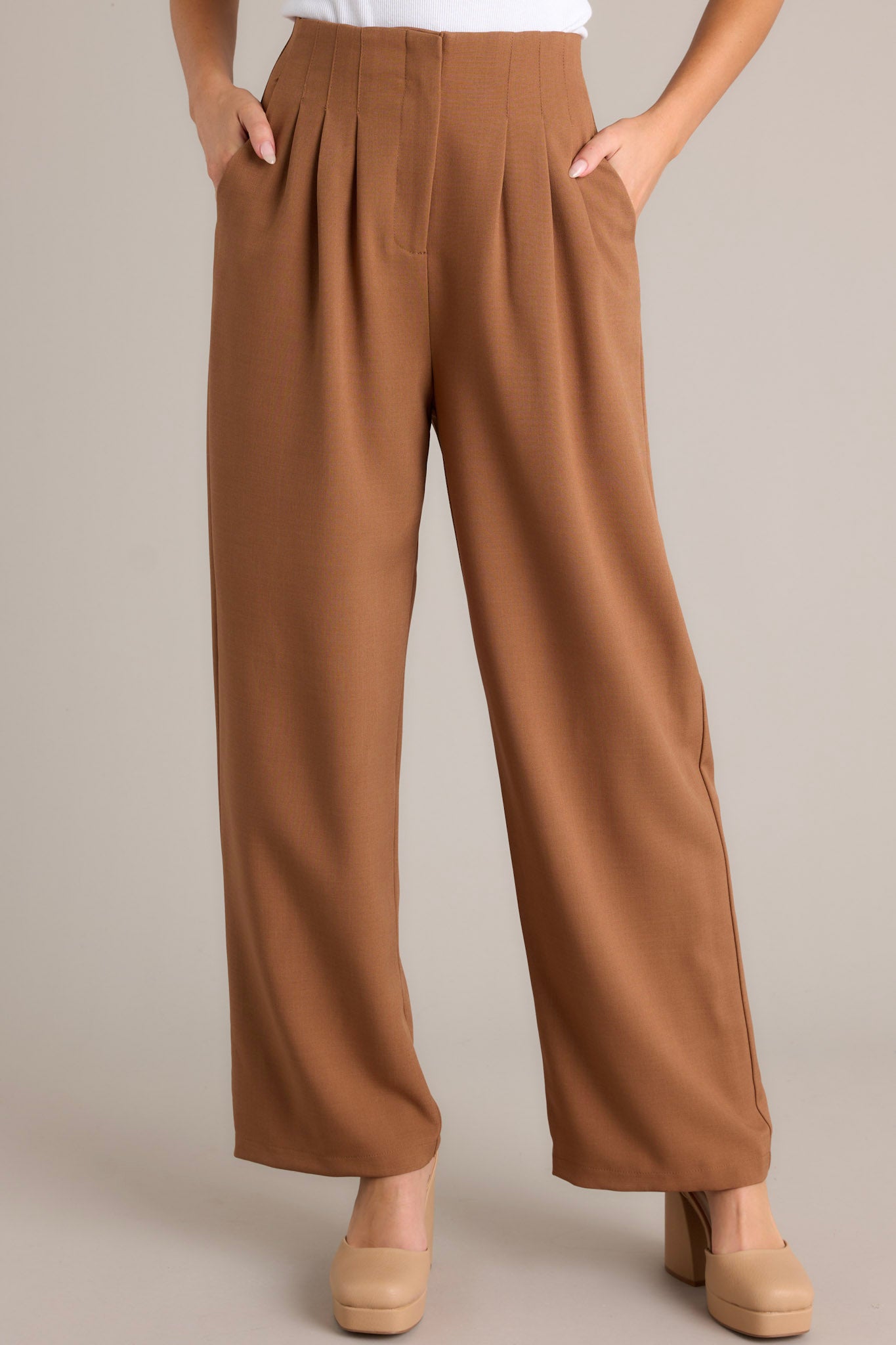 Front view of brown straight leg pants featuring a high waisted design, a button zipper closure, slight pleats, functional hip pockets, and a straight leg.