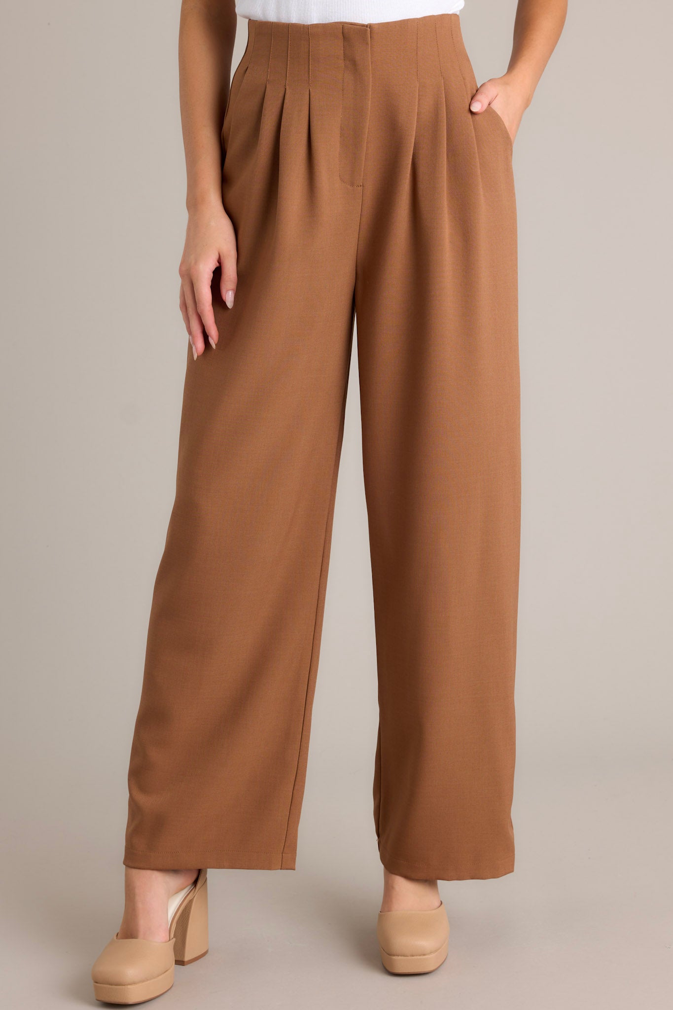 Front angled view of brown straight leg pants featuring a high waisted design, a button zipper closure, slight pleats, functional hip pockets, and a straight leg