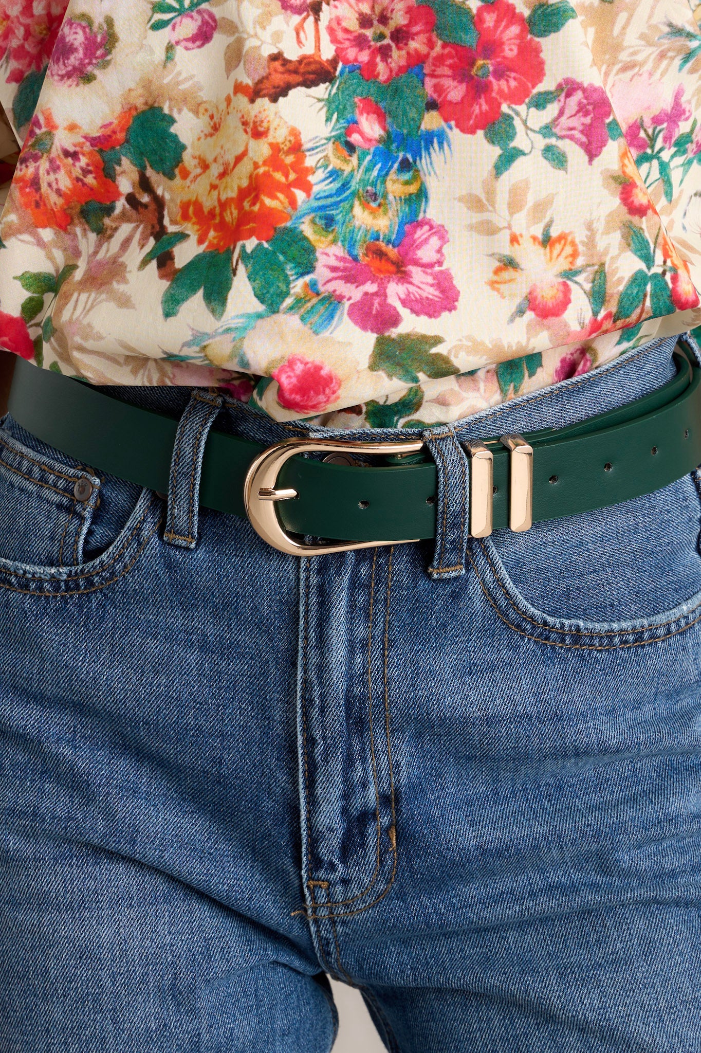 Close-up of this hunter green belt that features gold hardware buckle, a tan inside and two gold belt loops.