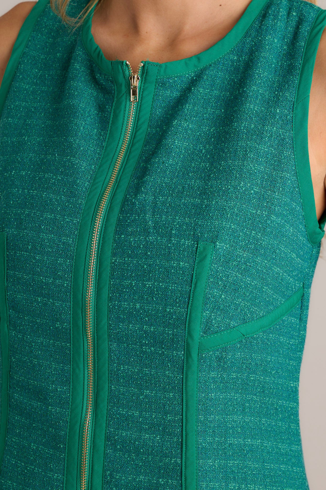 Close-up of a green mini dress showing the high crew neckline, functional zipper front, thick front seams, and the tweed material.