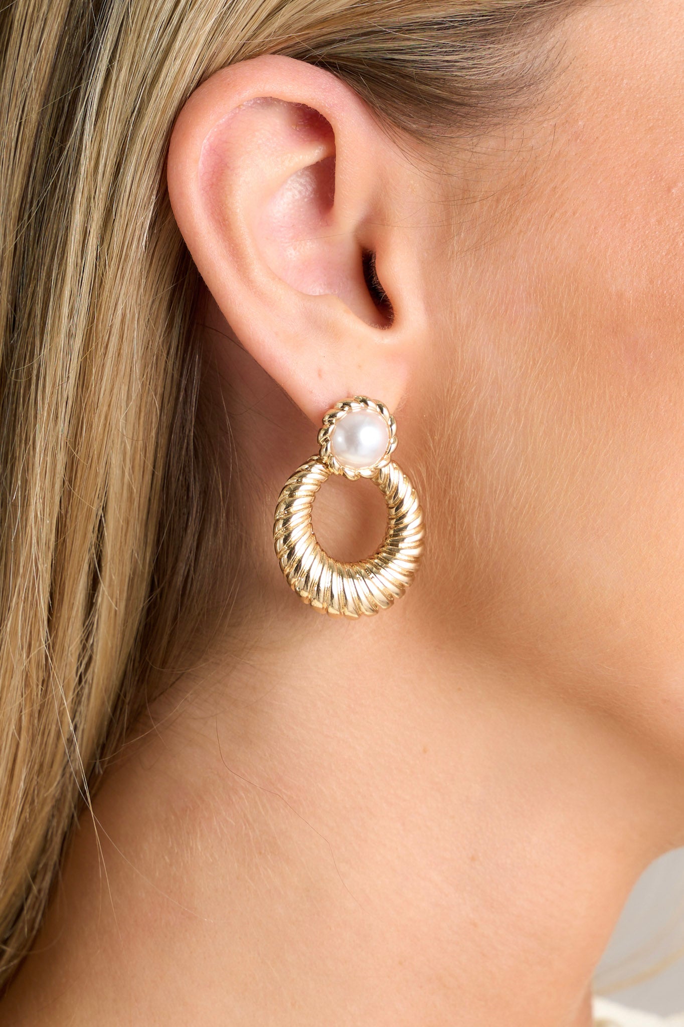 Close-up of these gold pearl hoops featuring a faux pearl stud surrounded in braided gold hardware, a gold textured hoop and secure post backings.