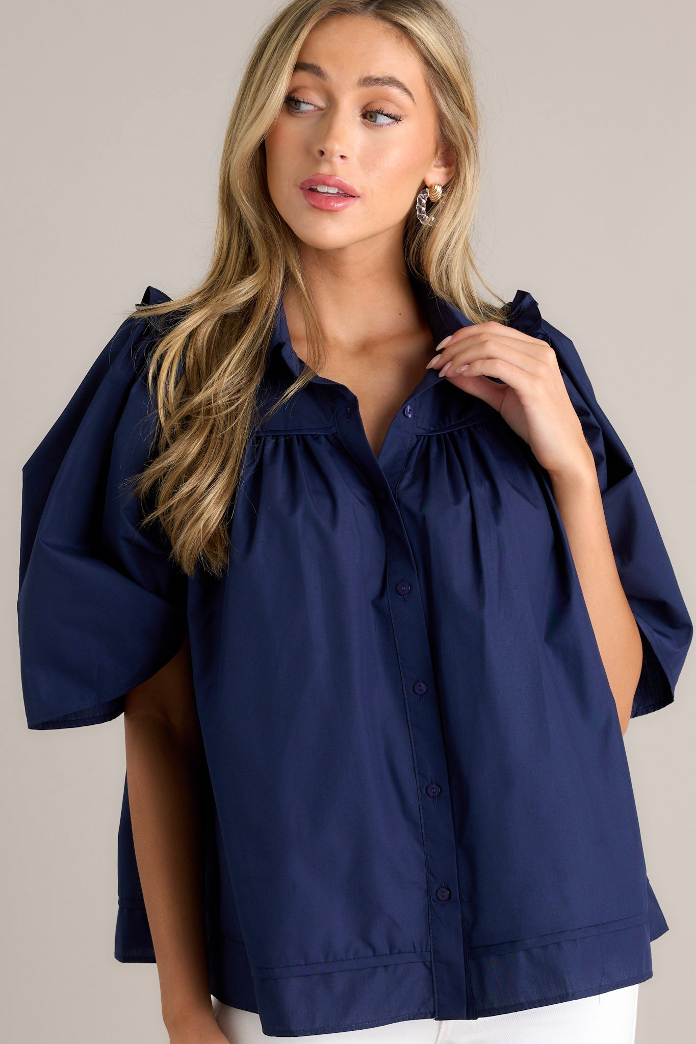 Front angled view of a navy top featuring a collared neckline, functional buttons down the front, butterfly short sleeves, and ruffle detailing.