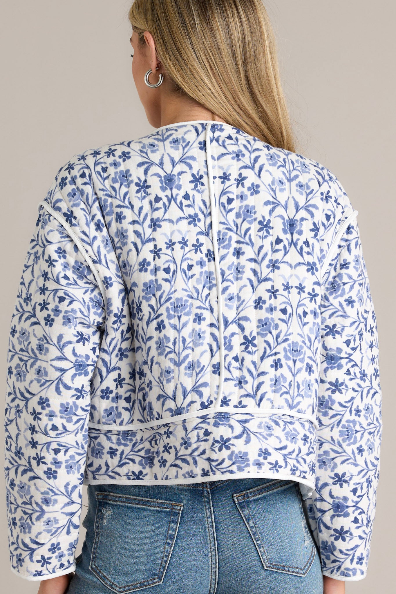 Back view of a blue jacket highlighting the overall floral print and the round neckline.