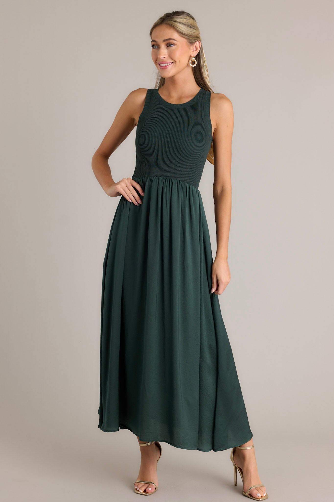 Full length view of a sweater top dress featuring a high rounded neckline, ribbed sweater bodice, lightly pleated skirt, a sleeveless design, and a flowing silhouette