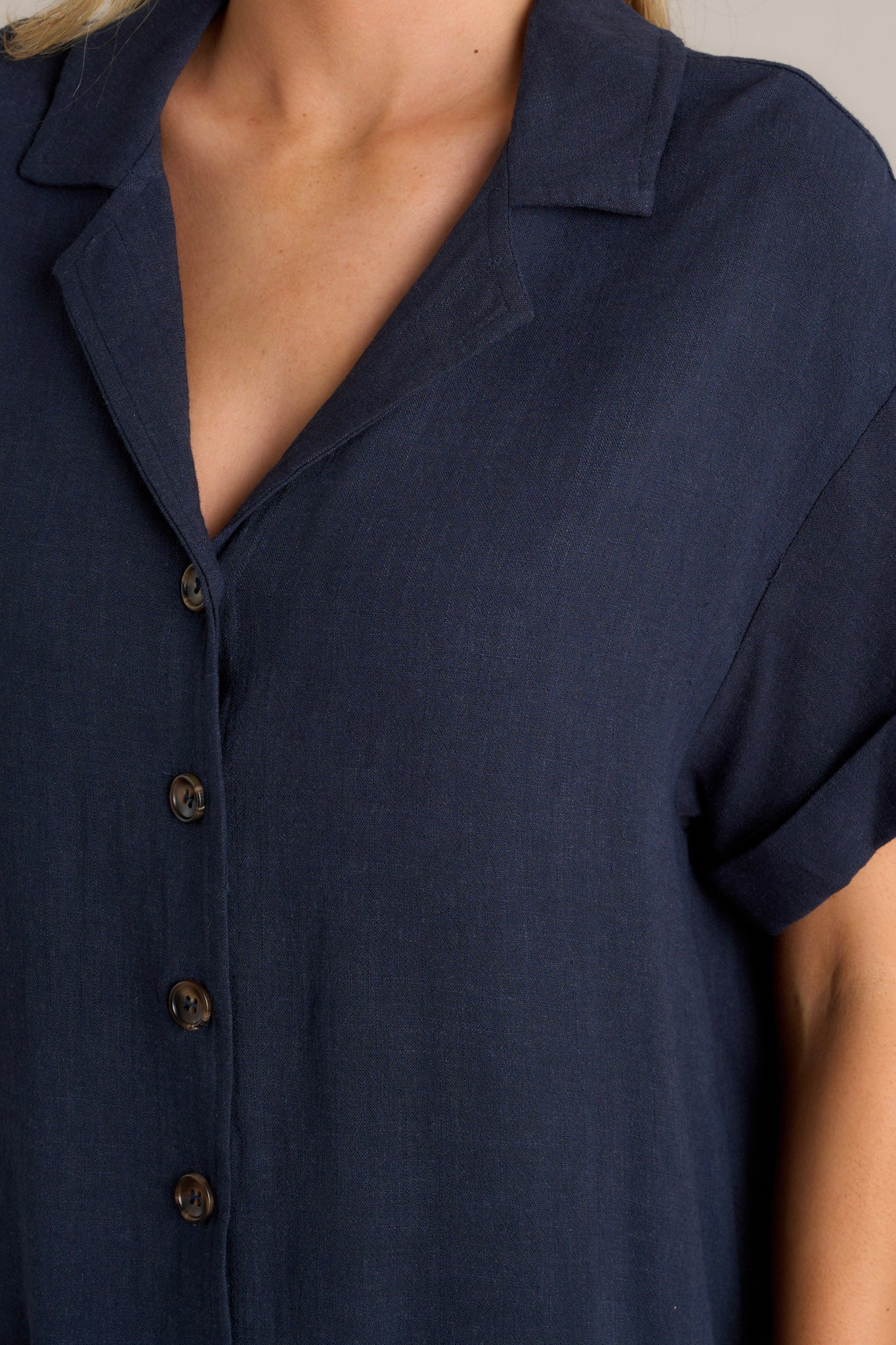 Close up view of this navy dress that features a collared neckline, functional button front, functional pockets, short cuffed sleeves and a relaxed fit.