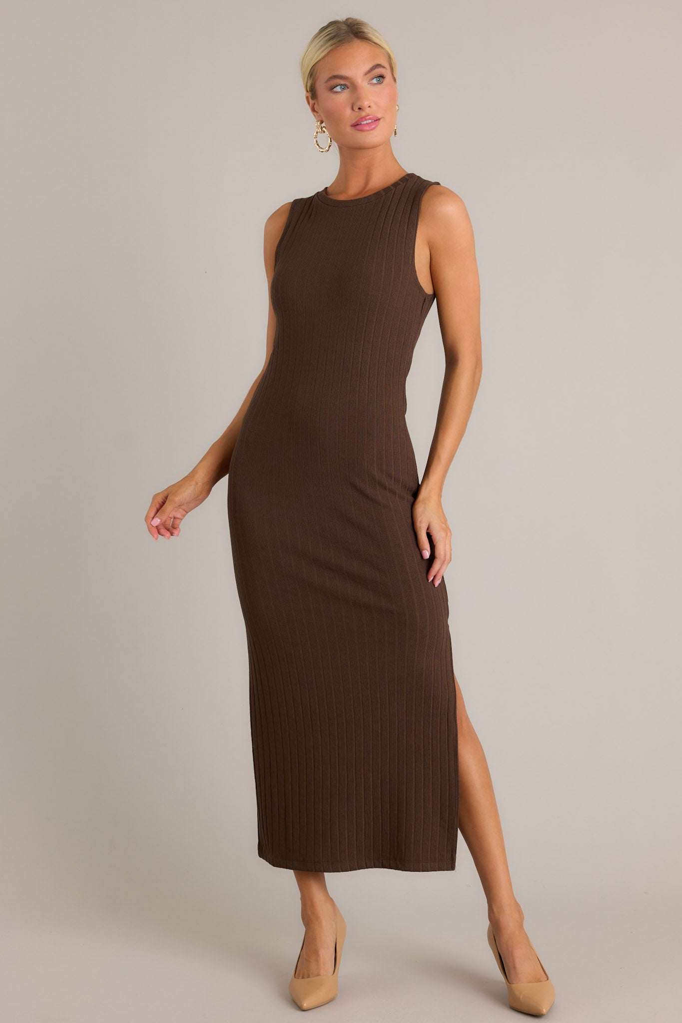 Front angled view of the brown dress featuring a high rounded neckline, a bodycon fit, soft ribbed fabric, a slit in the left leg, and a sleeveless design