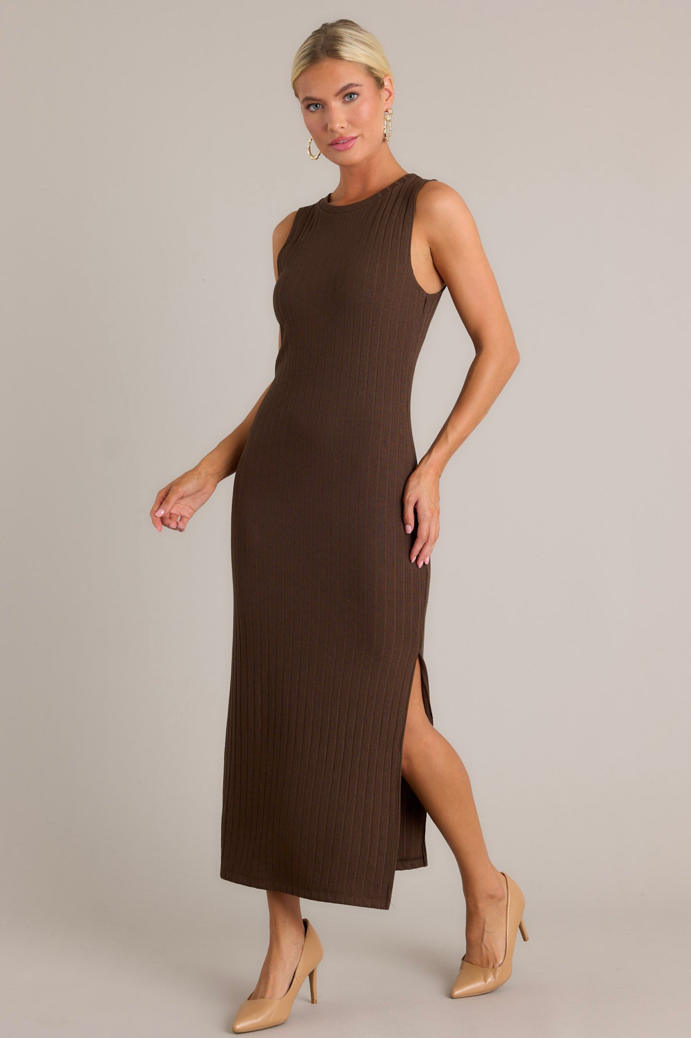 This brown dress features a high rounded neckline, a soft ribbed fabric, a bodycon fit, a slit in the left leg and a sleeveless design.