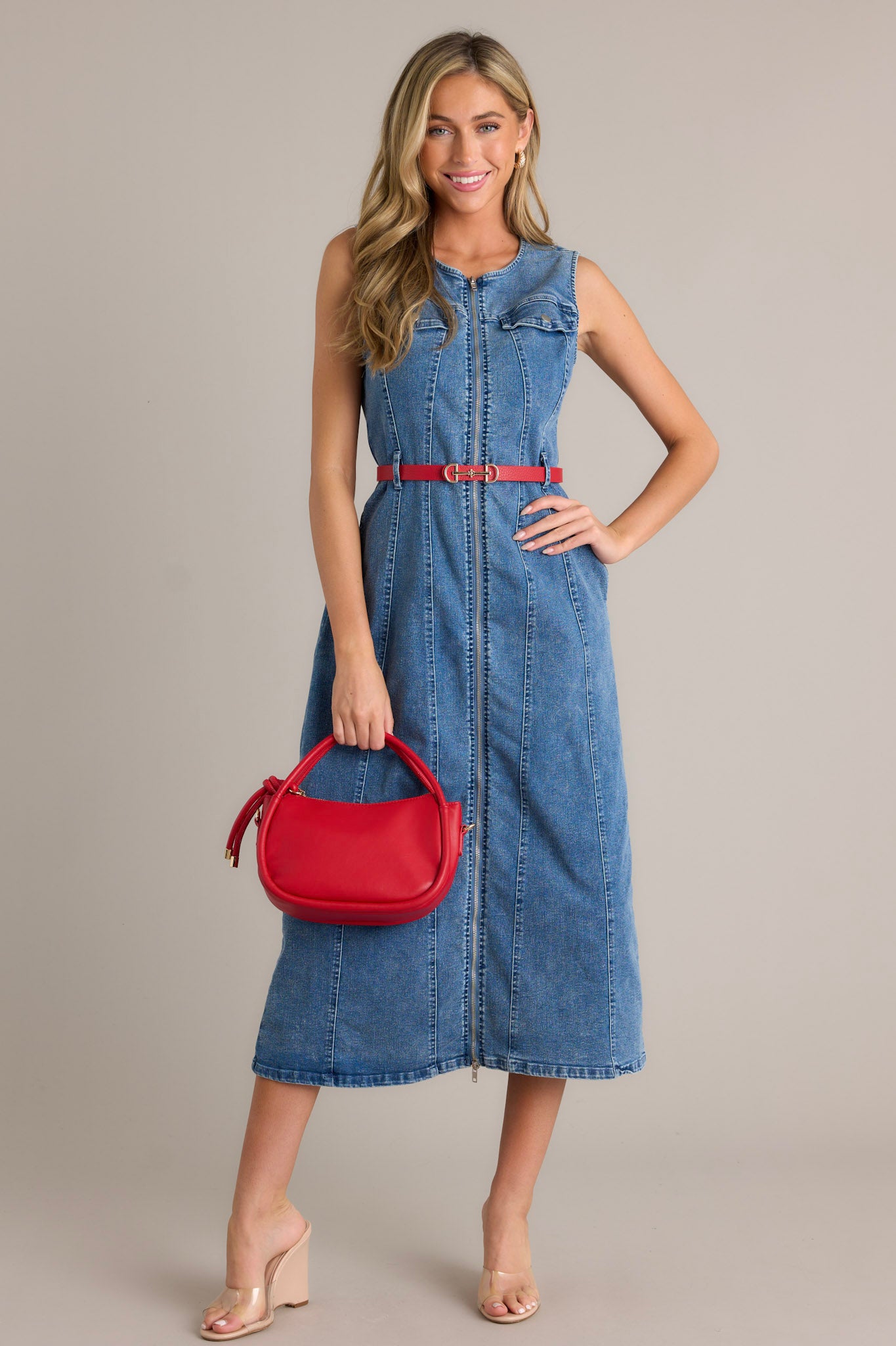 Full length view of a denim dress featuring a rounded neckline, functional front zipper, faux chest pockets, functional hip pockets, a self-tie denim drawstring belt, and a sleeveless design