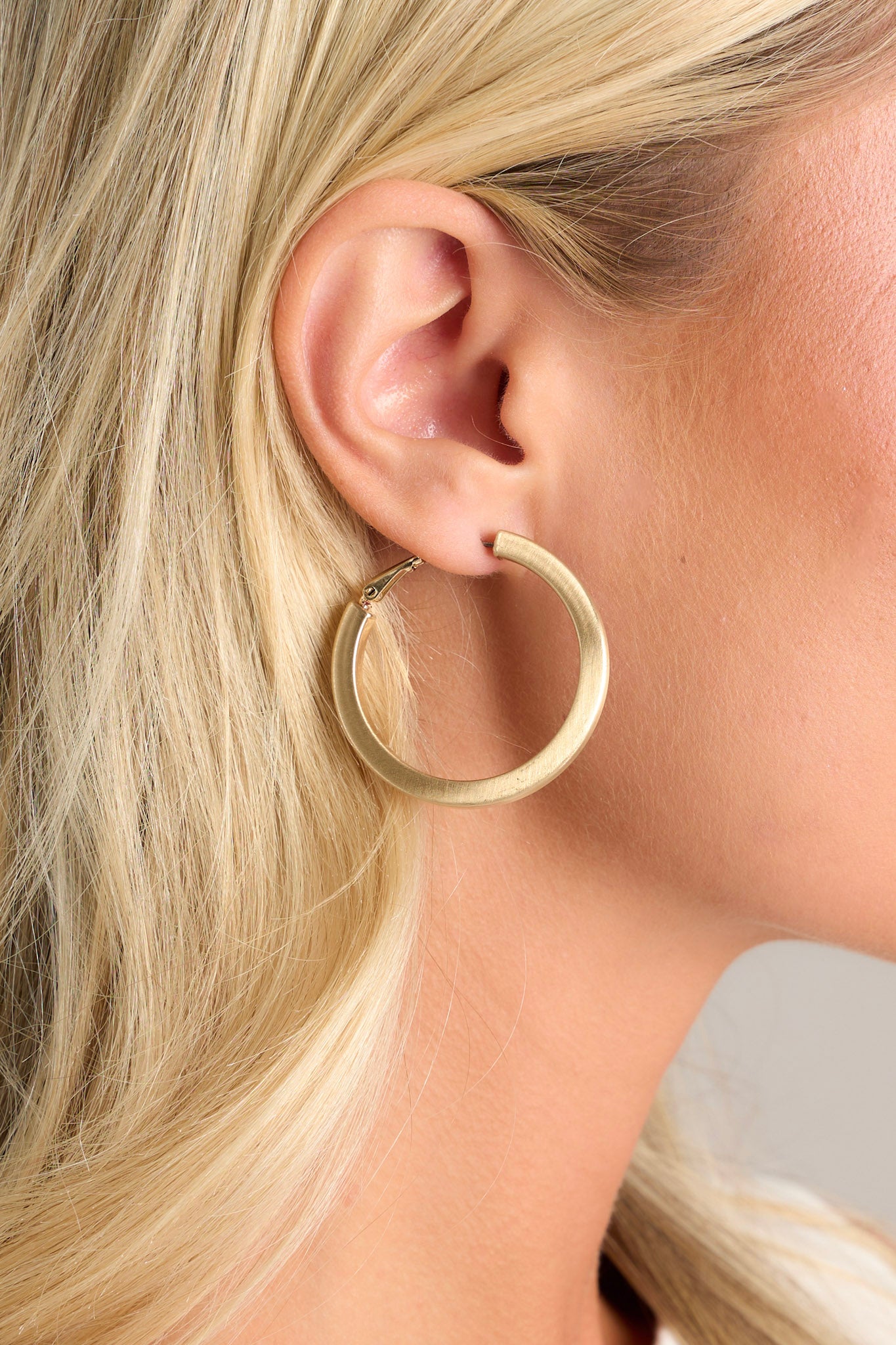 Close-up of these gold matte earrings that feature a thin design, gold hardware, and hinged hoop closure.