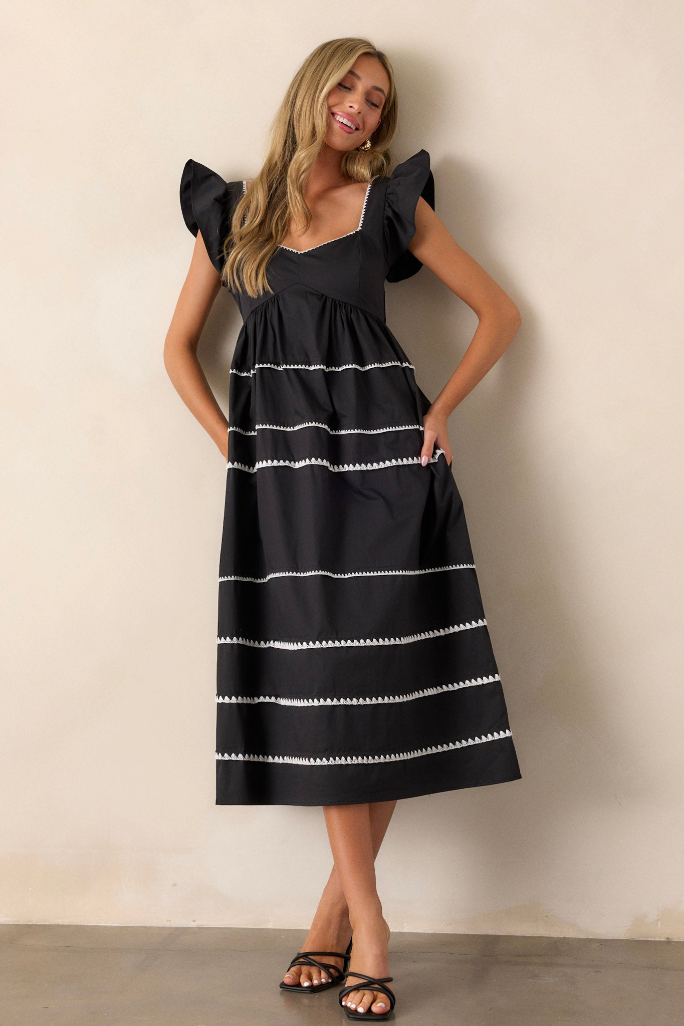 This black dress features ruffle cap sleeves, a smocked back, multiple tiers, two functional pockets, and ric-rac detailing.