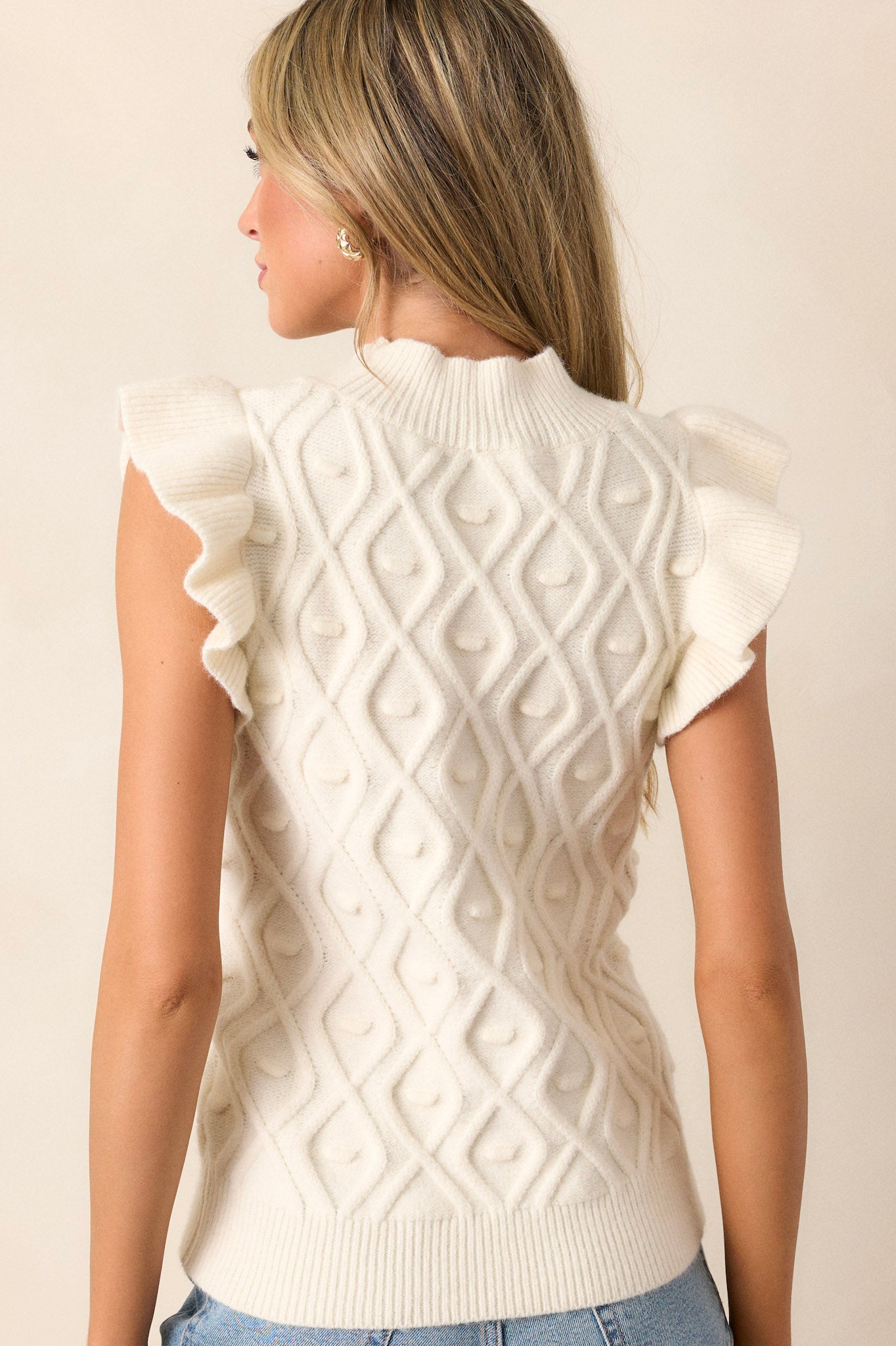 Back view of the ivory knit top highlighting the continuous diamond knitted design, the ribbed high neckline, and the thick ribbed hemline.