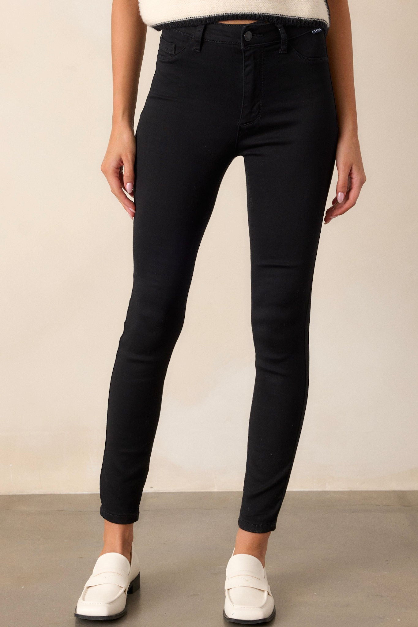 Front view of these black skinny jeans featuring a zipper and button closure, functional belt loops, and faux front pockets.