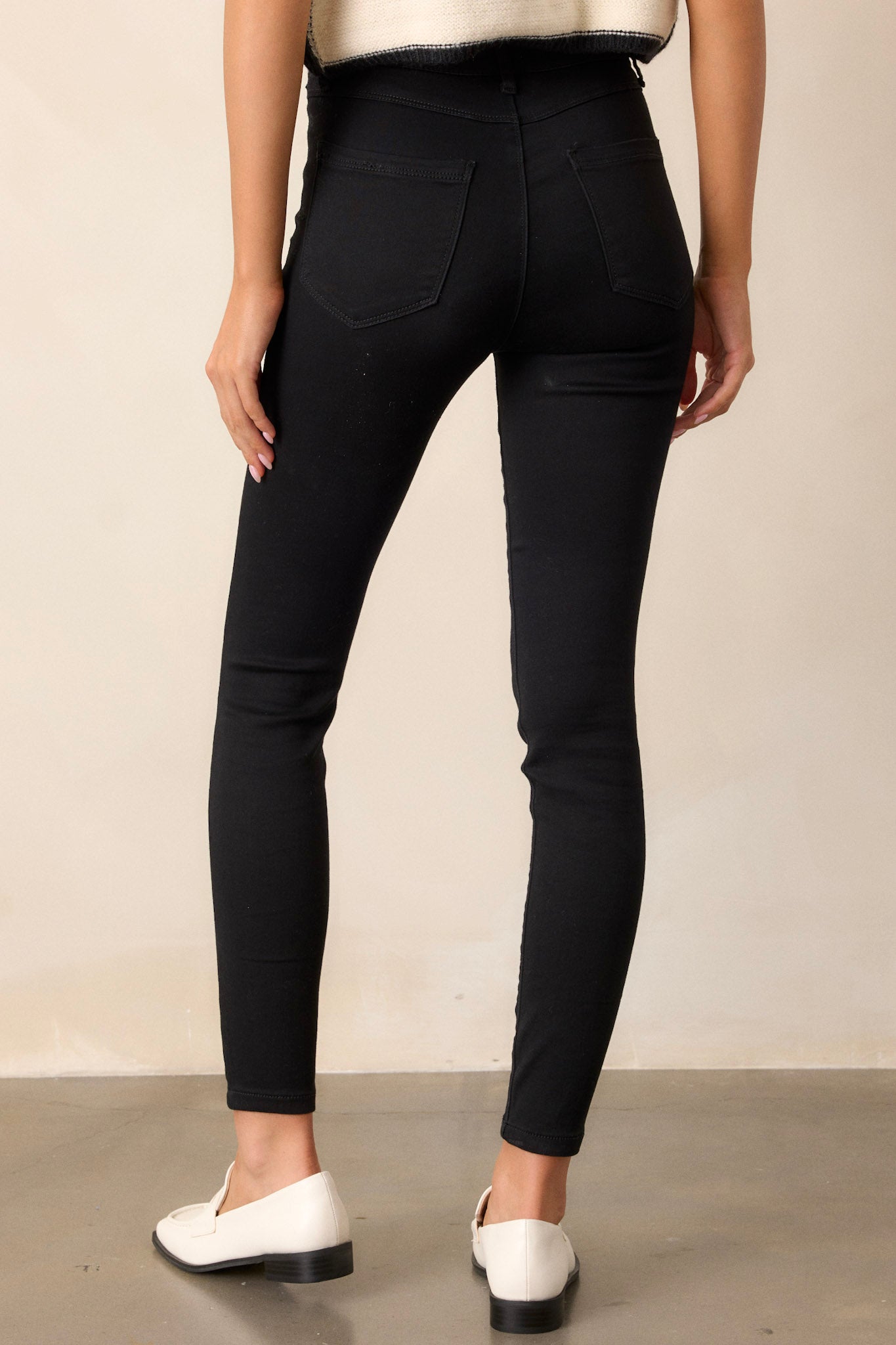 Back view of these black skinny jeans featuring a zipper and button closure, functional belt loops, and faux front pockets.