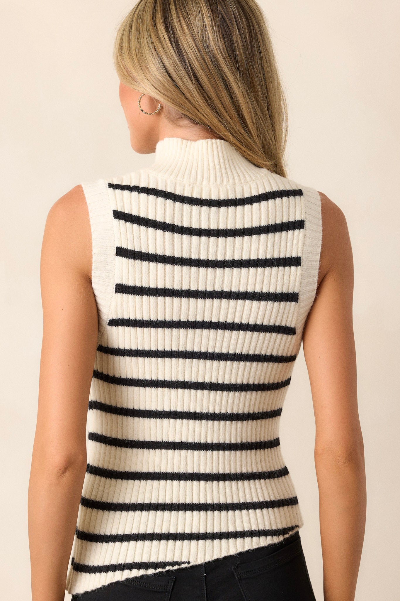 Back view of this ivory top featuring a high neck design, a ribbed knit texture, a sleeveless design, and a slightly cropped length.