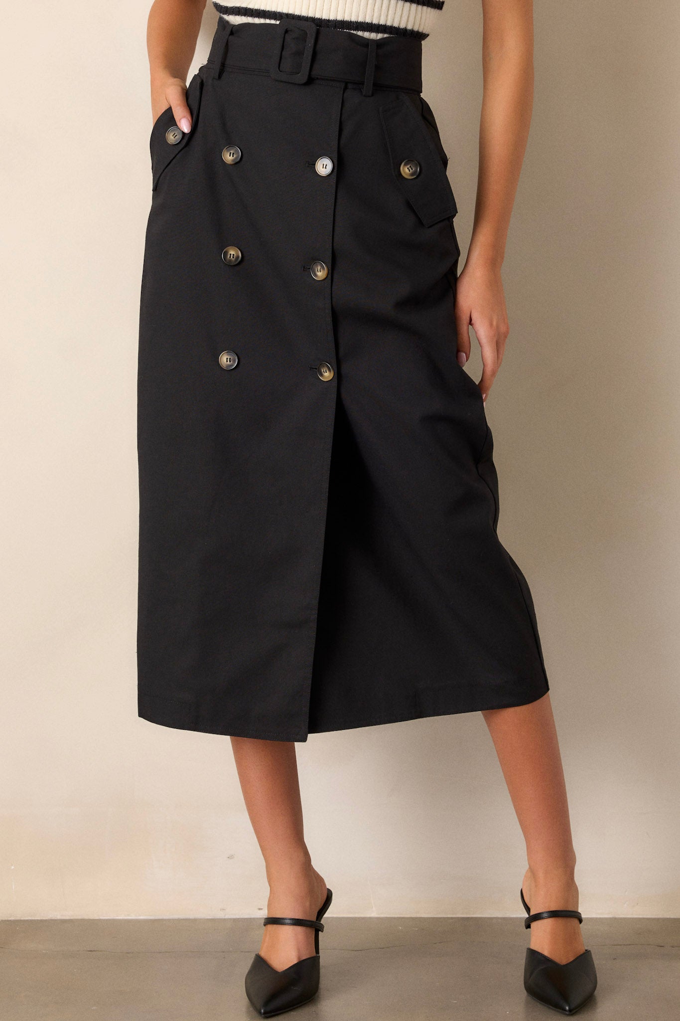 Front angled view of a black maxi skirt featuring a high waisted design, an elastic waist insert, a square fabric belt, functional hip pockets, functional front buttons, and an open leg