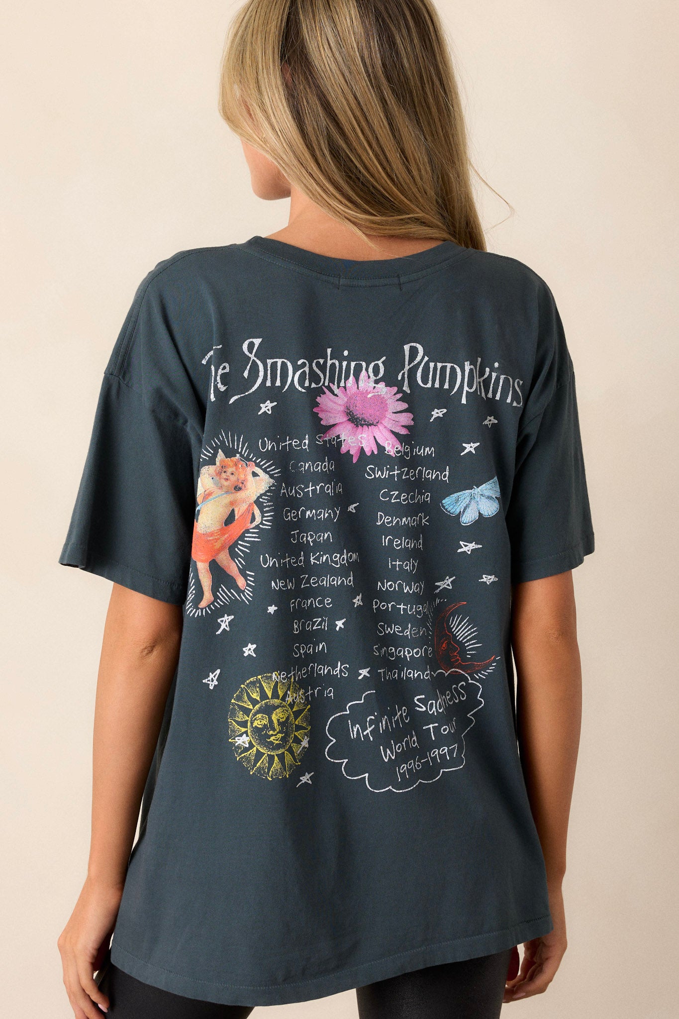 Back view of a black graphic tee featuring short sleeves, a crew neckline, "The Smashing Pumpkins" with artwork inspired by their album cover on the front, and a list of their anticipated tour stops on the back.