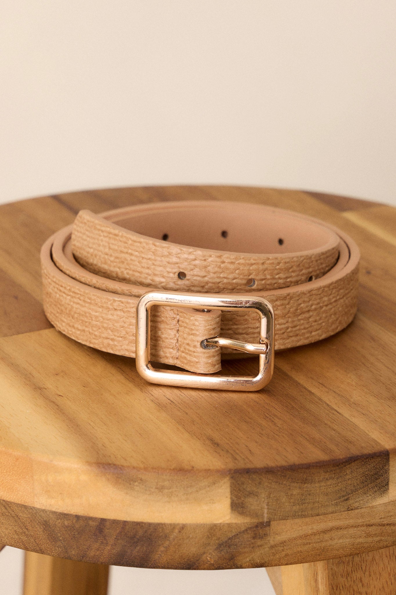 Close-up of this tan belt that features a woven texture, a gold square buckle, and a single prong