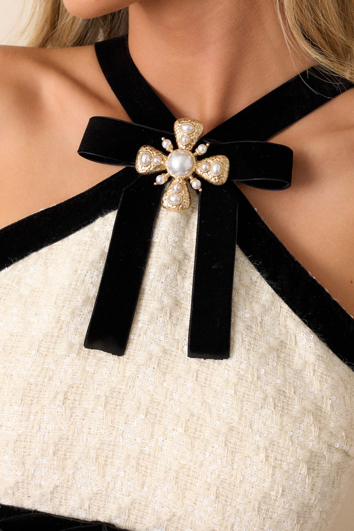 Close-up of the ivory halter dress focusing on the tweed material, clear sequined glitter decoration, and the faux black waist belts with bows.