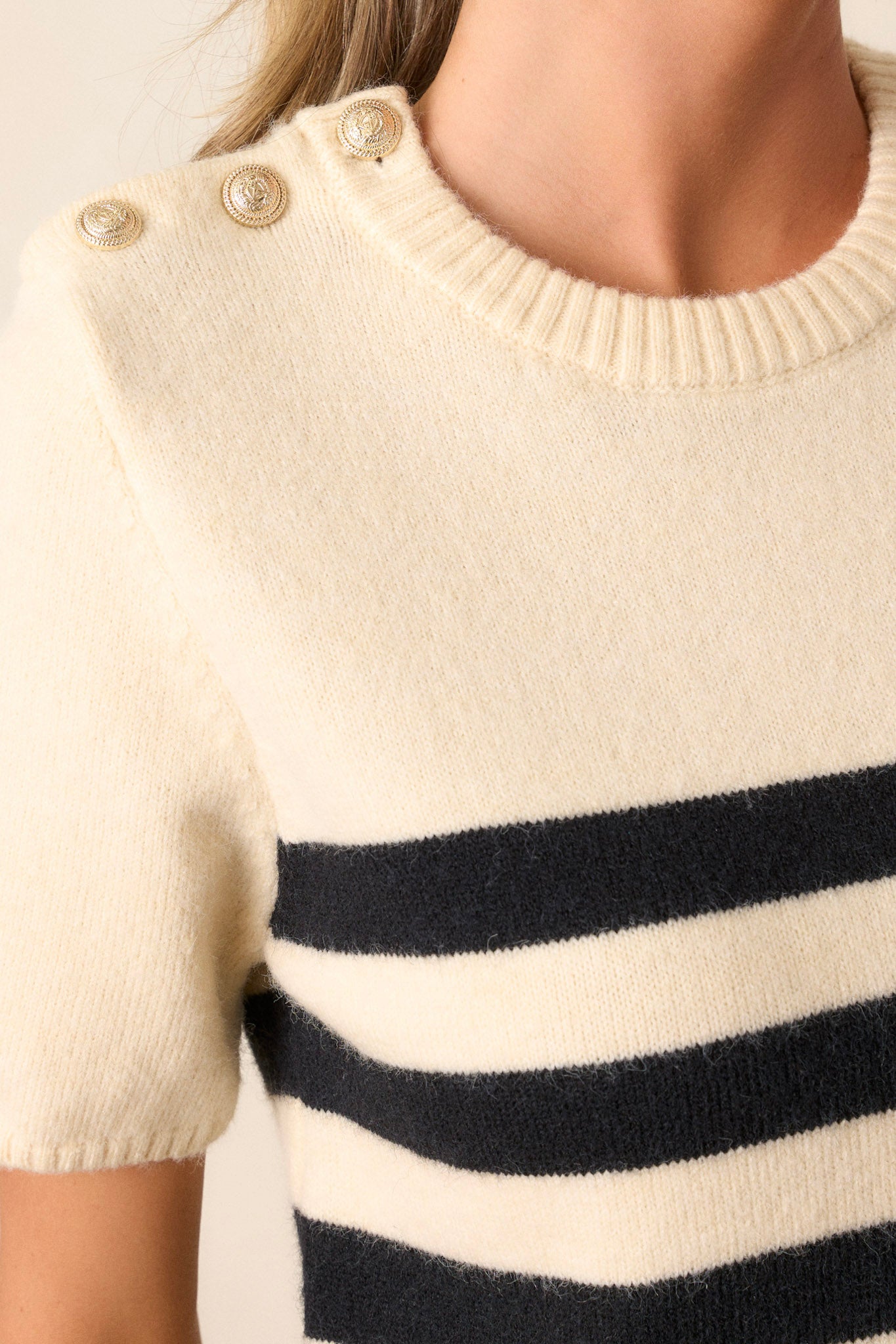 Detailed shot of the gold buttons on the shoulder of this beige sweater top. 