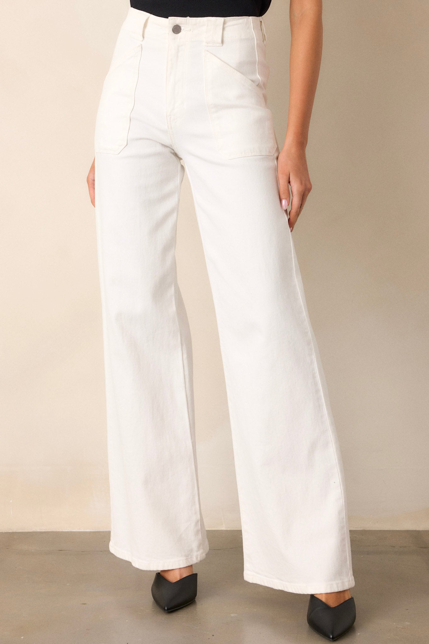 Close up view of these white jeans that feature a high waisted design, classic button & zipper closure, belt loops, functional front patch pockets, and a flare leg.