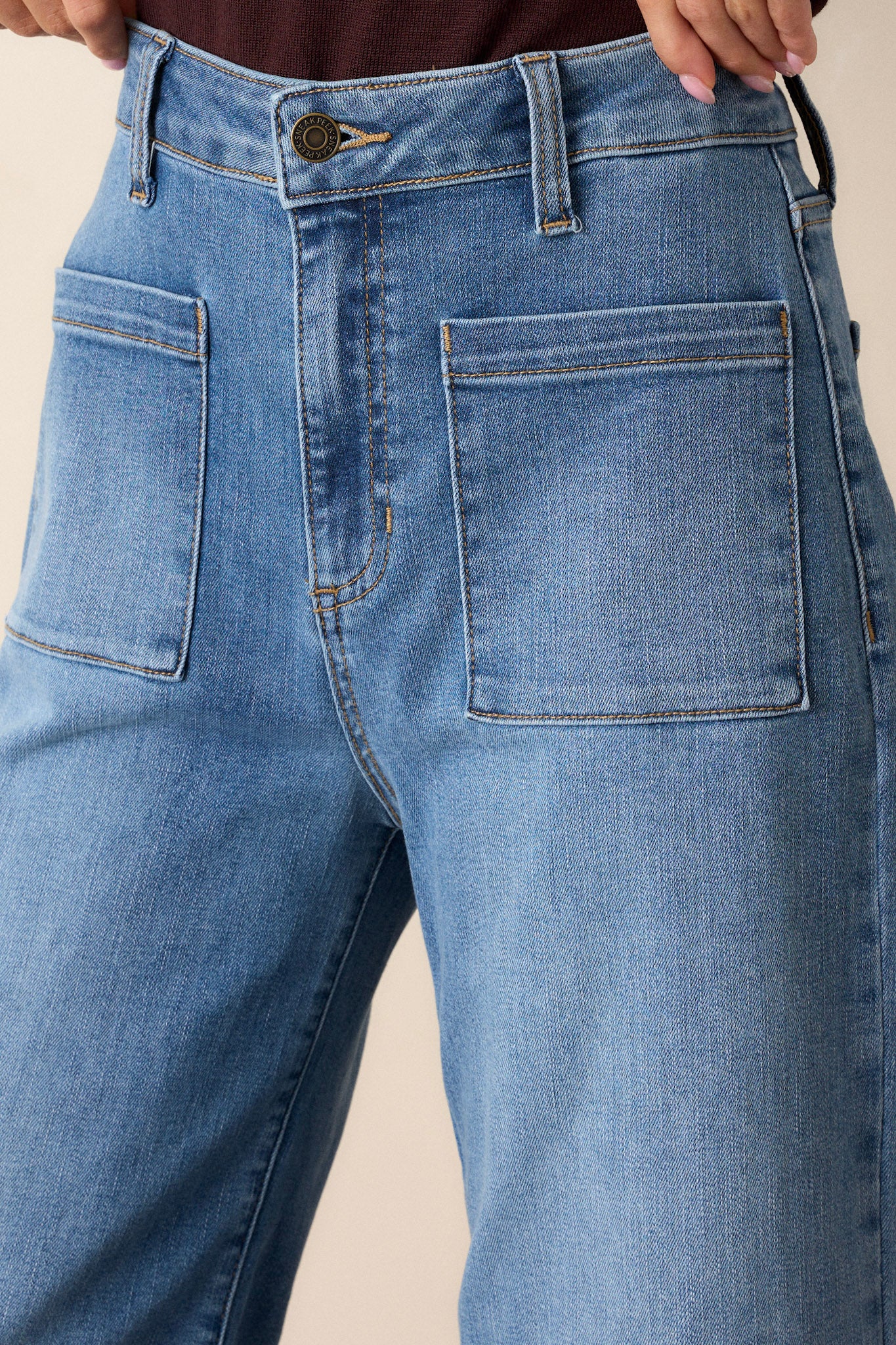 Close-up of the medium wash jeans focusing on the button zipper closure, belt loops, and the texture of the denim fabric.