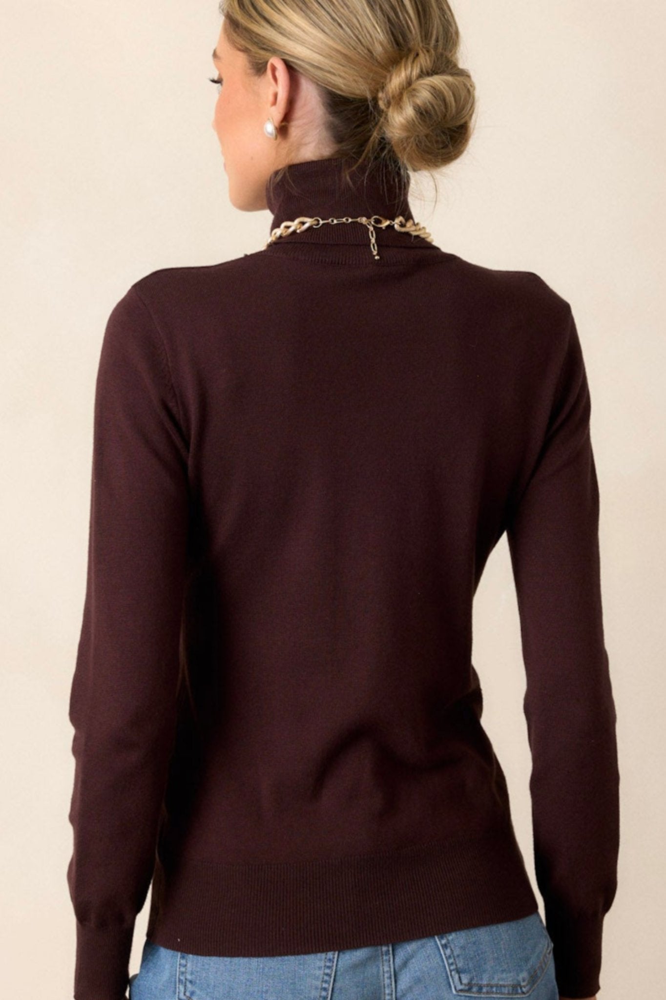 Back view of the sweater highlighting the turtle neckline, the smooth back panel, and the tapered ribbed bottom hem