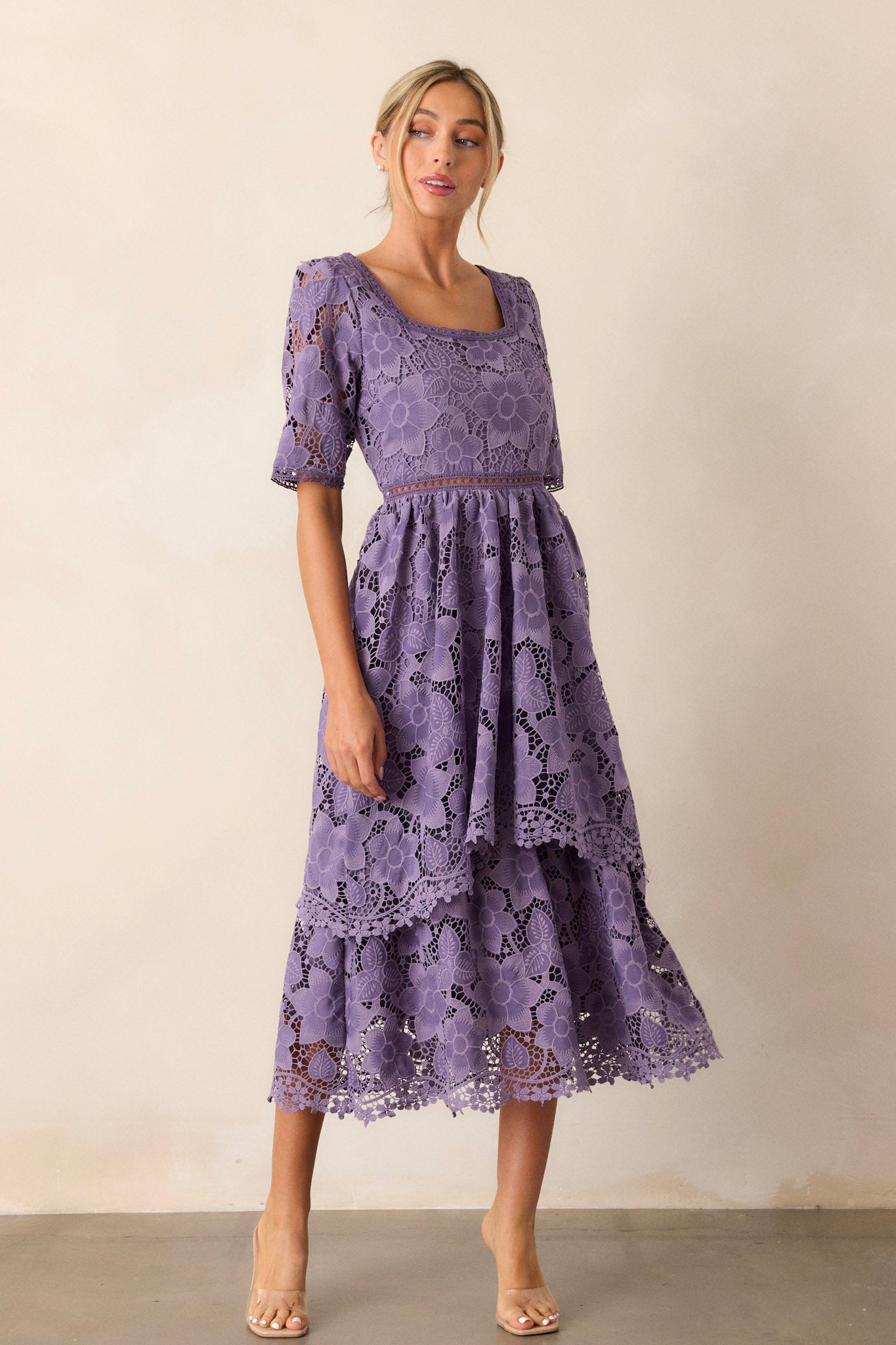 Full-length view of a model wearing the lilac dress, emphasizing the square neckline, lace floral design, lace cutout waist design, tiered skirt, and half sleeves.