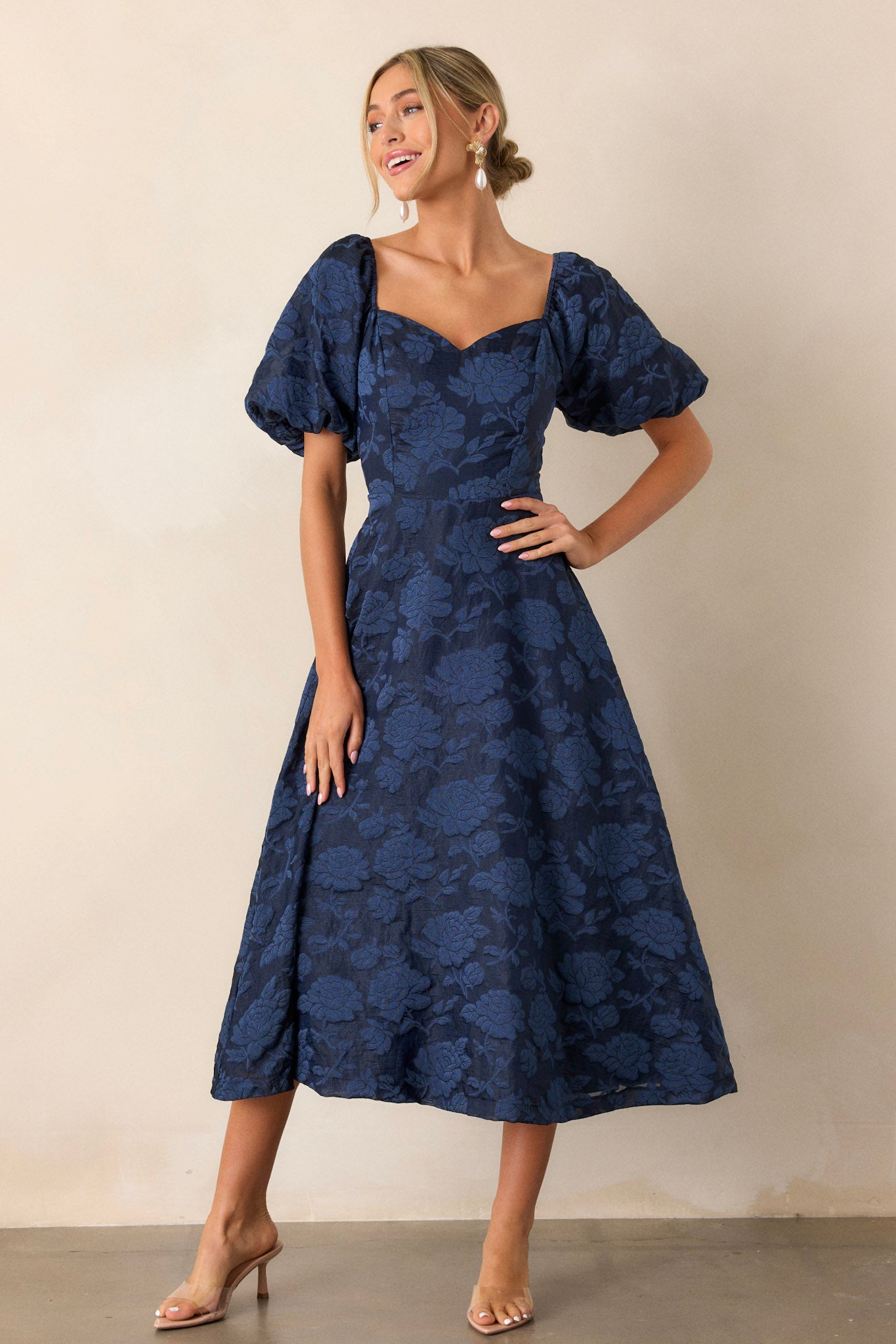 Front view of a navy floral dress featuring a Queen Anne neckline, a fitted bodice, and elastic cuffed puff sleeves