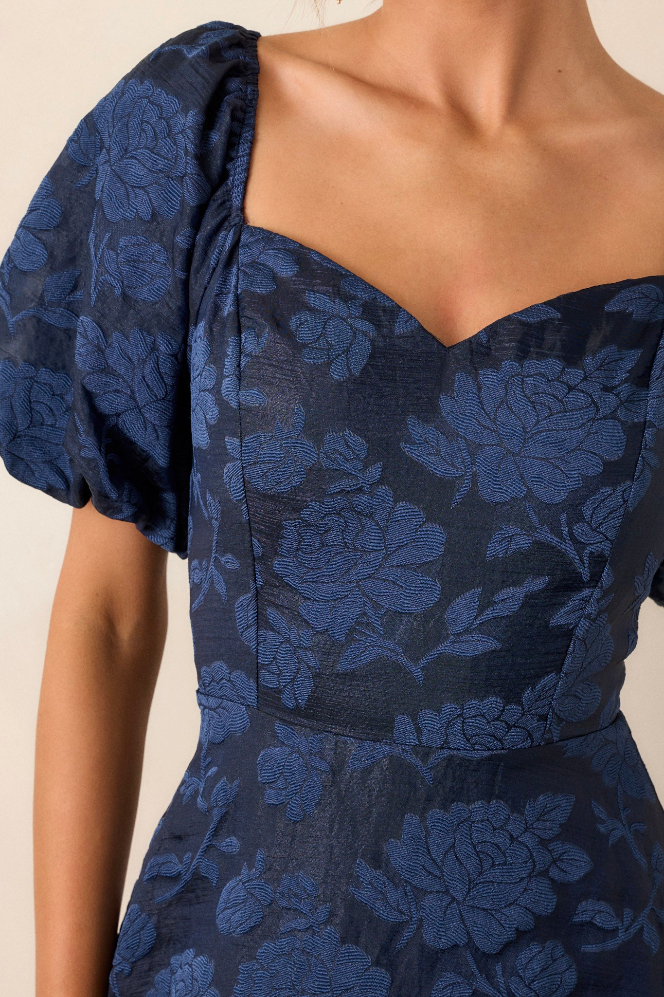 Close-up of the navy floral dress focusing on the Queen Anne neckline, floral design, and the detailing of the fitted bodice and elastic cuffed puff sleeves.