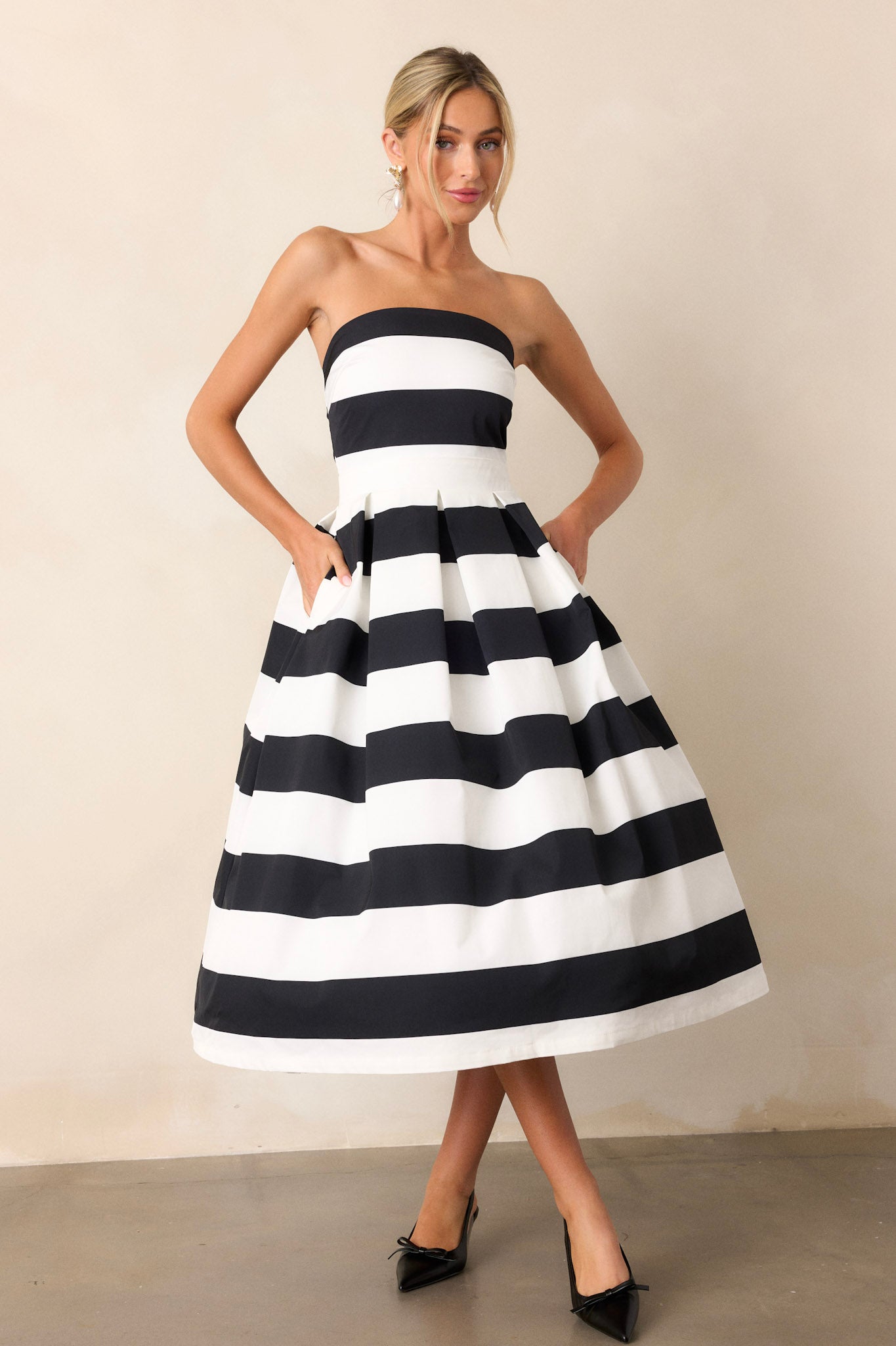 Full-length view of a model wearing the dress, emphasizing the strapless neckline, thick waistband, functional hip pockets, and the timeless stripe pattern