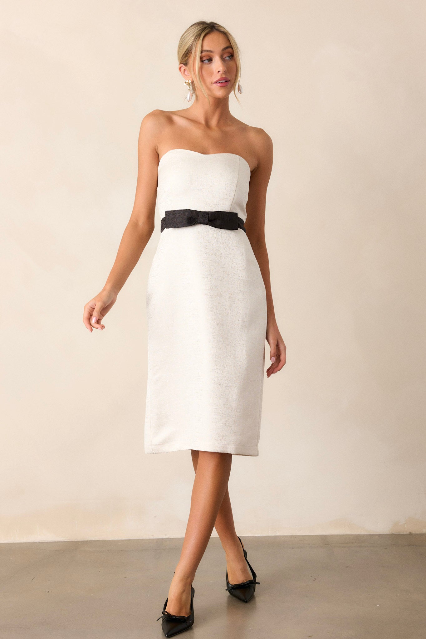 Front angled view of the dress featuring a sweetheart neckline, black faux waist belt with a bow, small slit in the back hem, and strapless design