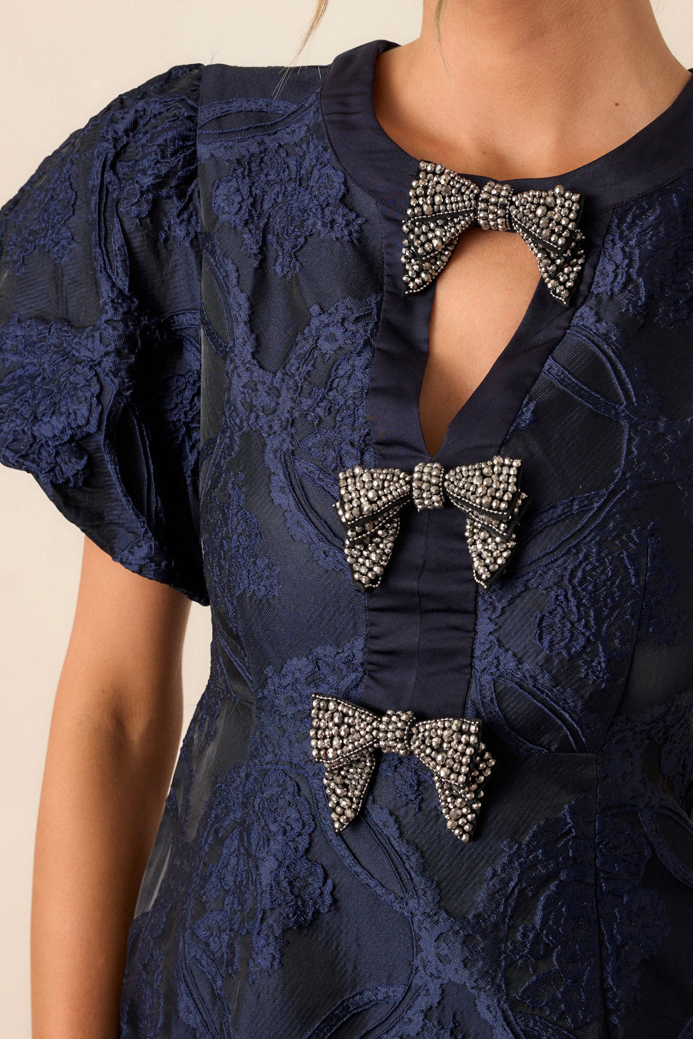 Close-up of the navy dress focusing on the high neckline, triangular cutout, and the intricate bow details on the bodice.