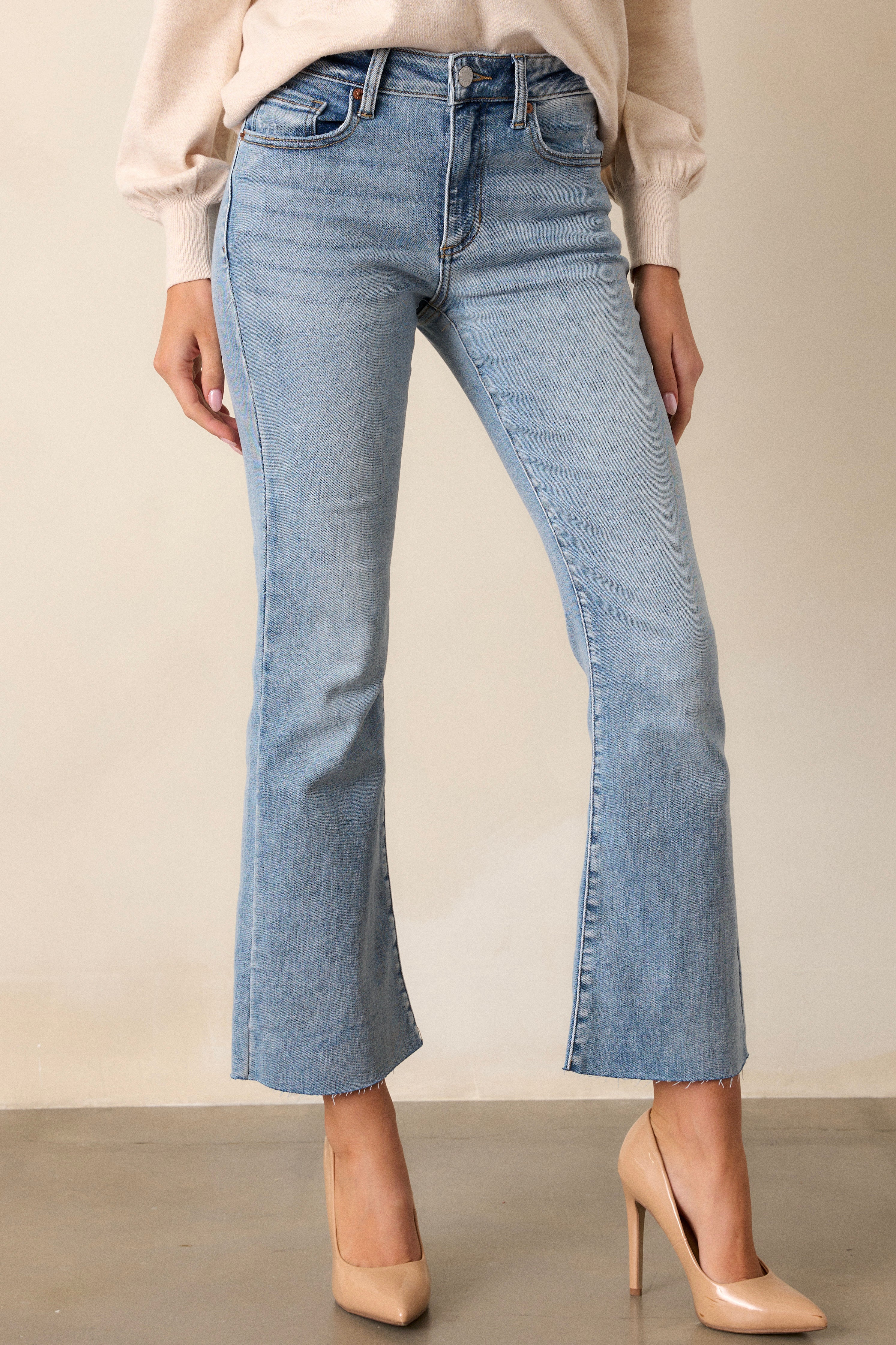 Front angled view of the pants featuring a high waisted design, functional hip and back pockets, functional belt loops, a light washed denim, a button zipper closure, and a cropped flare leg,