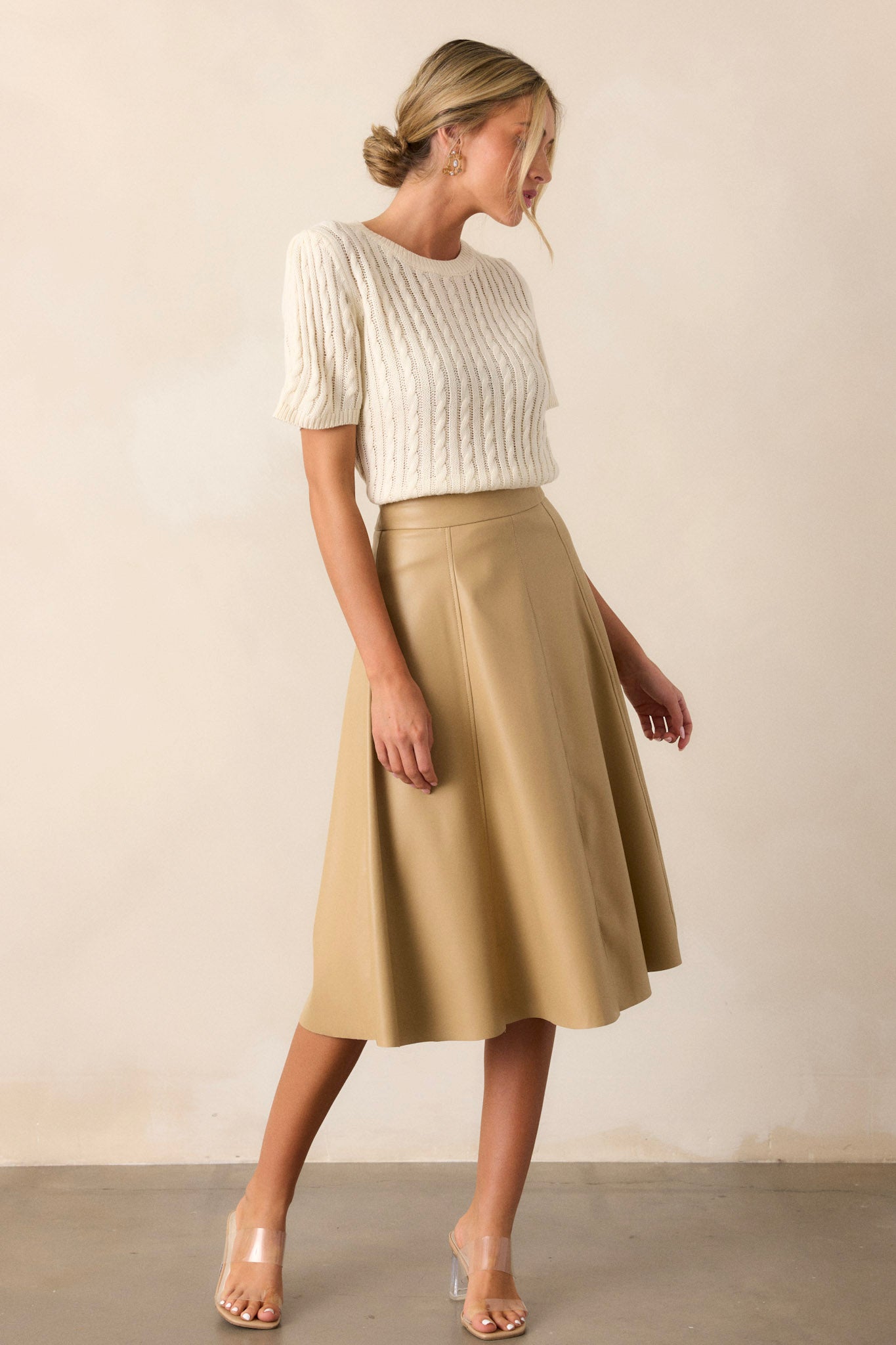 Full-length view of a model wearing the skirt, displaying the A-line design, stitch detailing on the seams, side zipper, and the rich faux leather fabric.