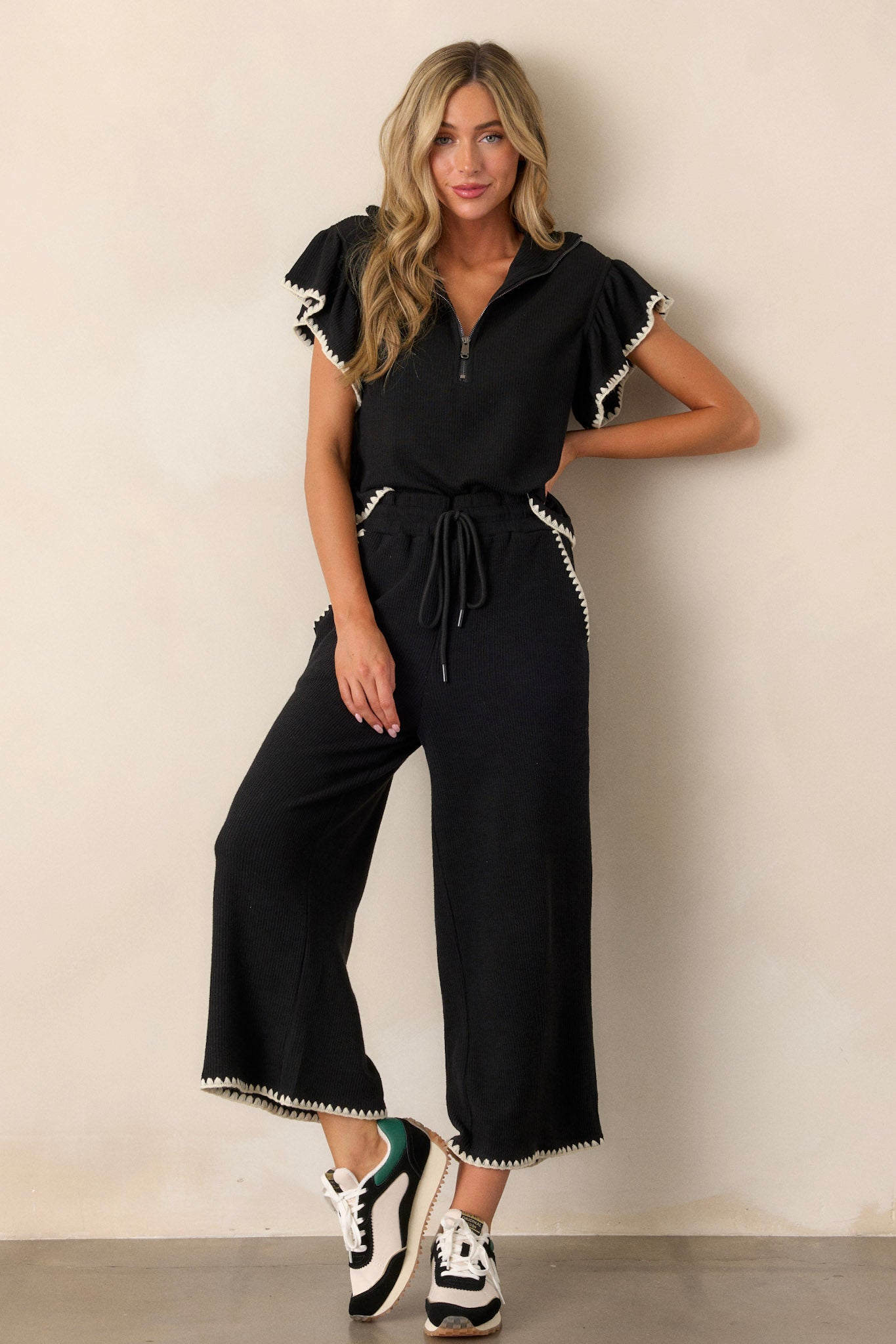 Full body of these black pants that feature an elastic waistband, an optional waist drawstring, an ivory ruffle trim, functional hip pockets, a soft stitched material and a wide leg