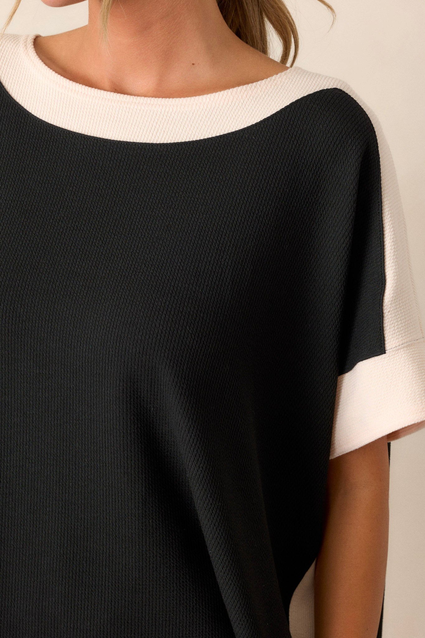 Close-up of the black and ivory top focusing on the ivory trim along the off-the-shoulder neckline, arms, and sides, as well as the slight ribbed texture of the fabric