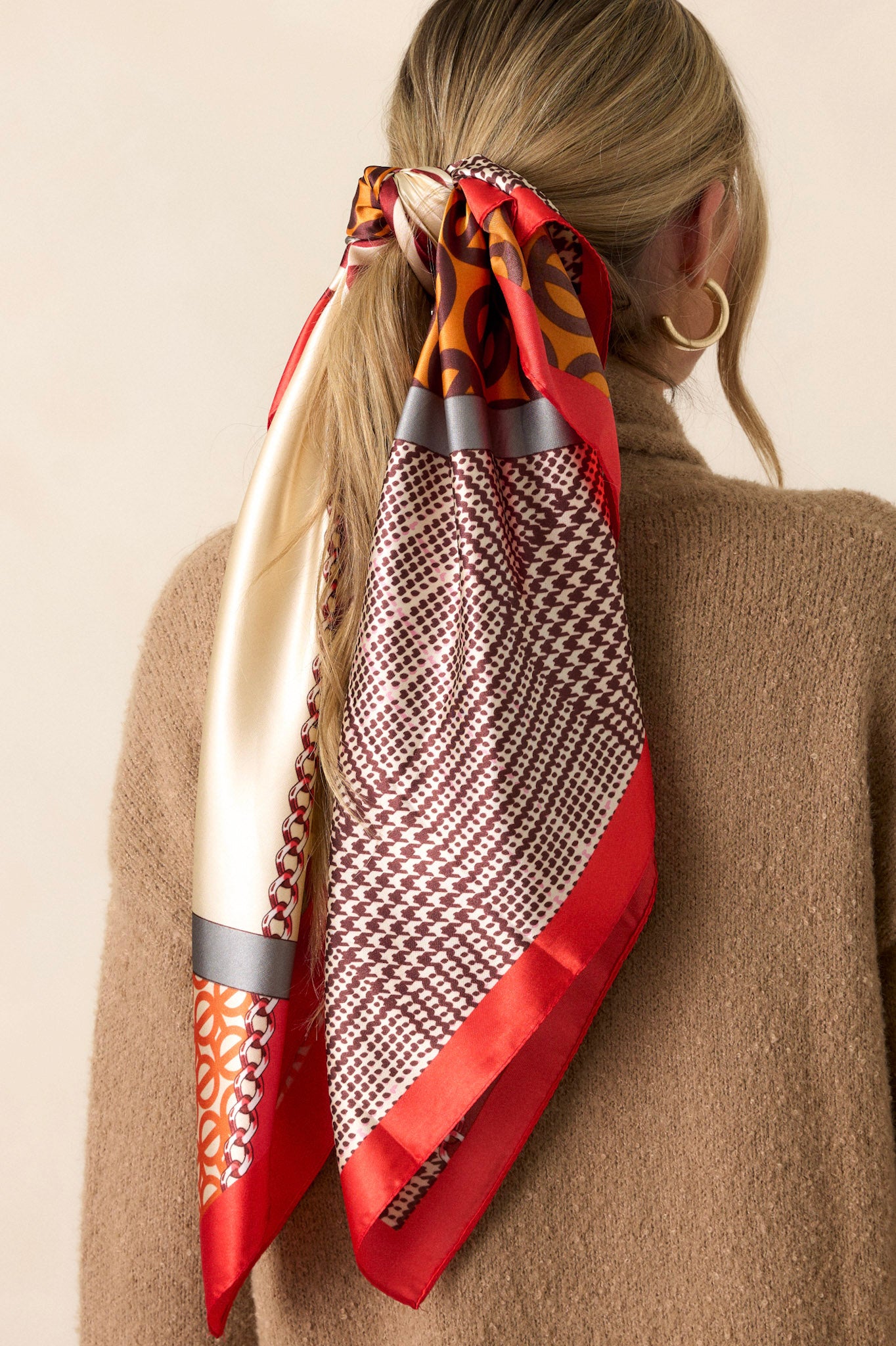 Close-up view of this Red scarf that features a red trim, with multi print designs, and a silky feel