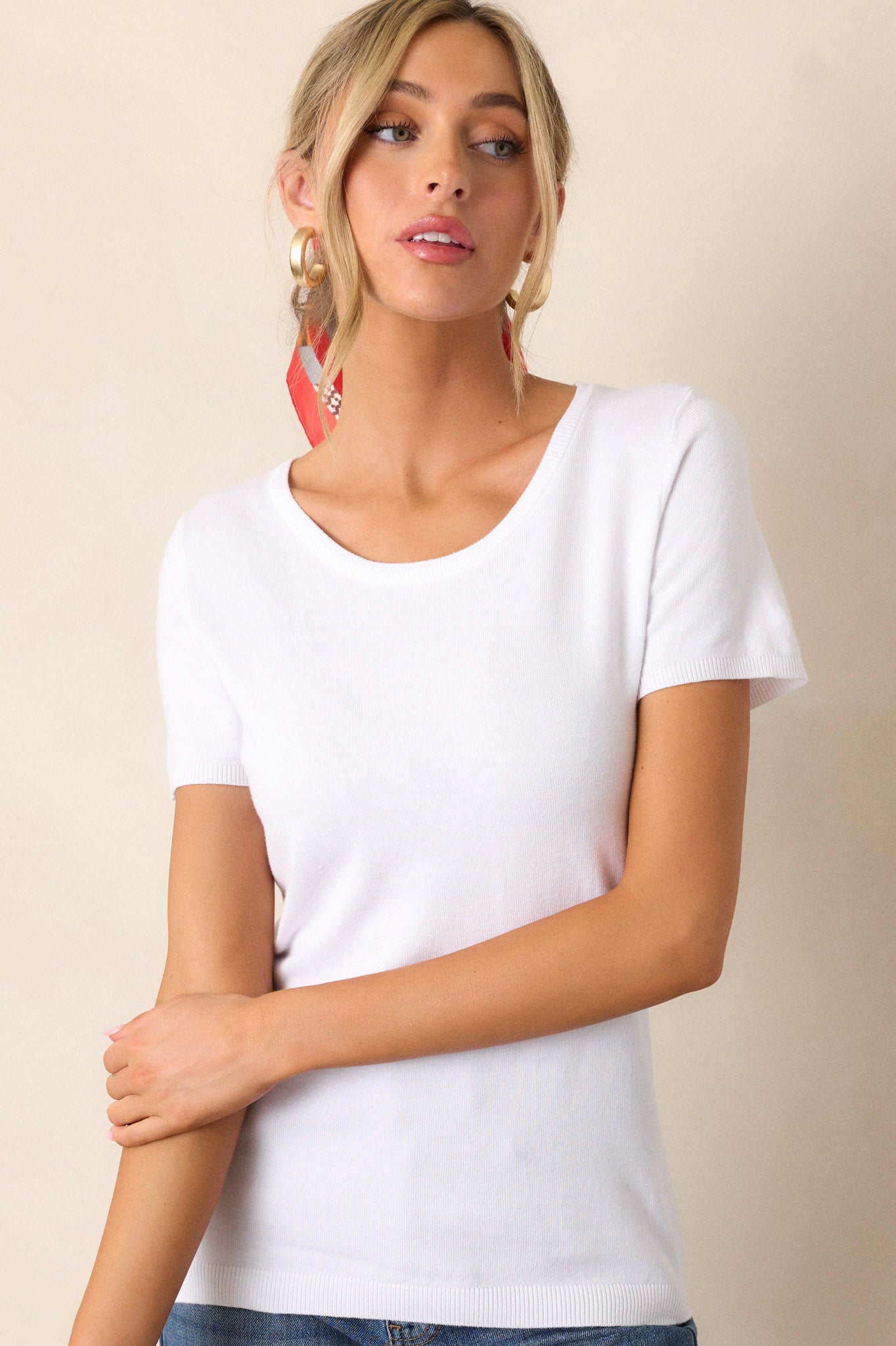 Front view of a white sweater top featuring a rounded neckline, a soft sweater fabric, a ribbed hem, and short sleeves