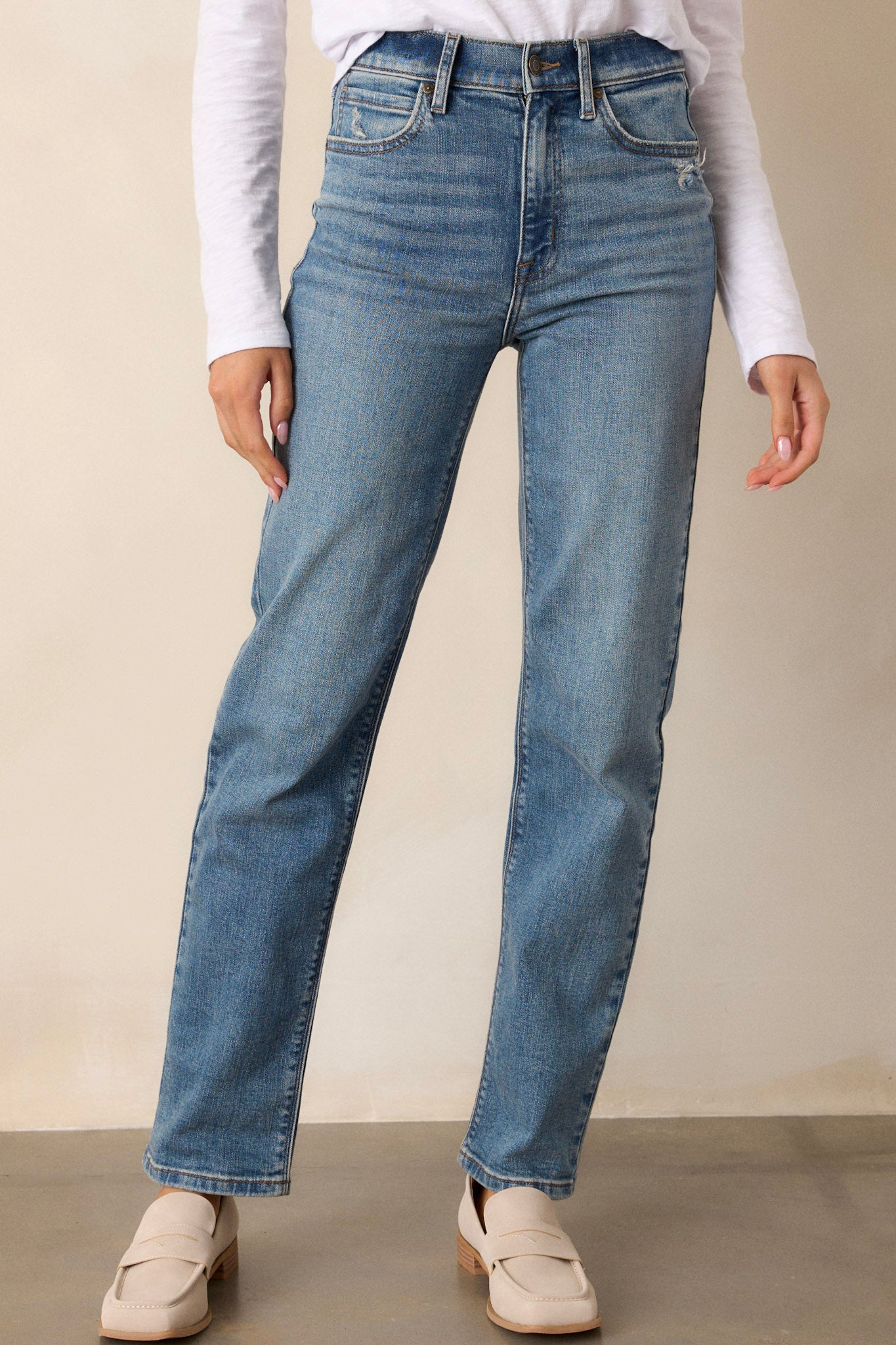 Front angled view of medium wash straight leg jeans featuring a high waist design, functional front & back pockets, distressed pocket detailing, a button & zipper closure, and a straight leg