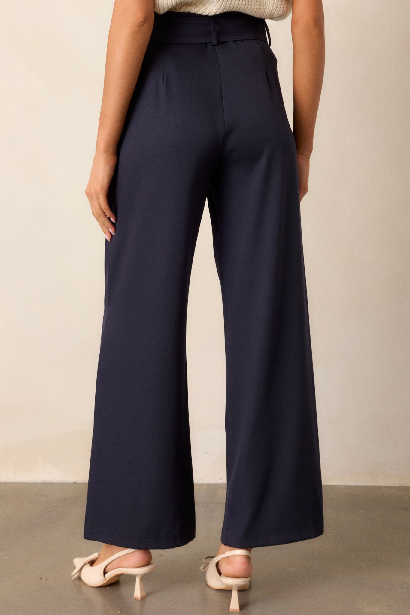 Back view of navy belted pants highlighting the high waisted design, functional back pockets, and wide leg.