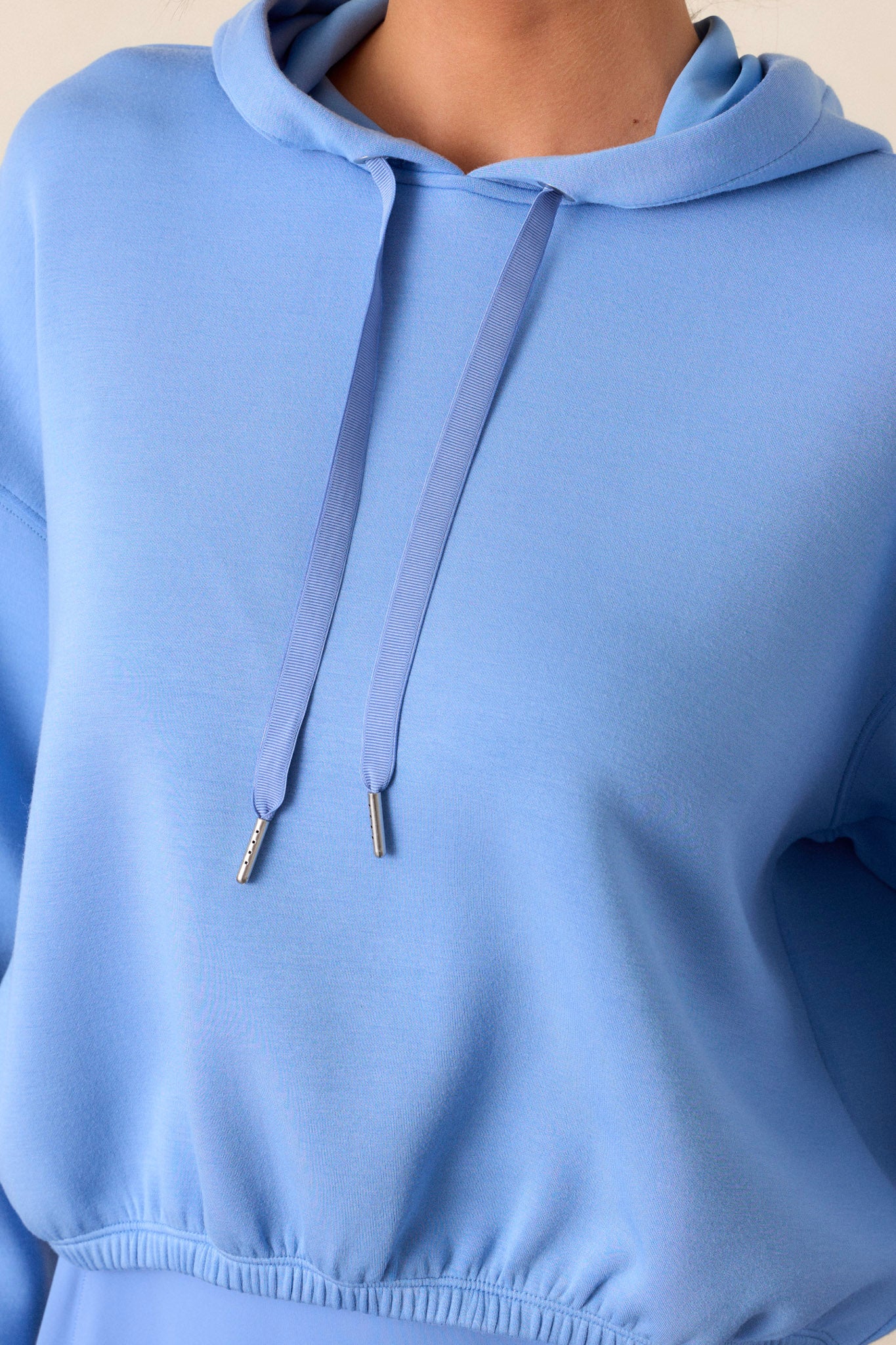 Close-up of the cornflower blue hoodie focusing on the finely knit fabric, elastic hem, and the high neckline, highlighting the texture and detailing