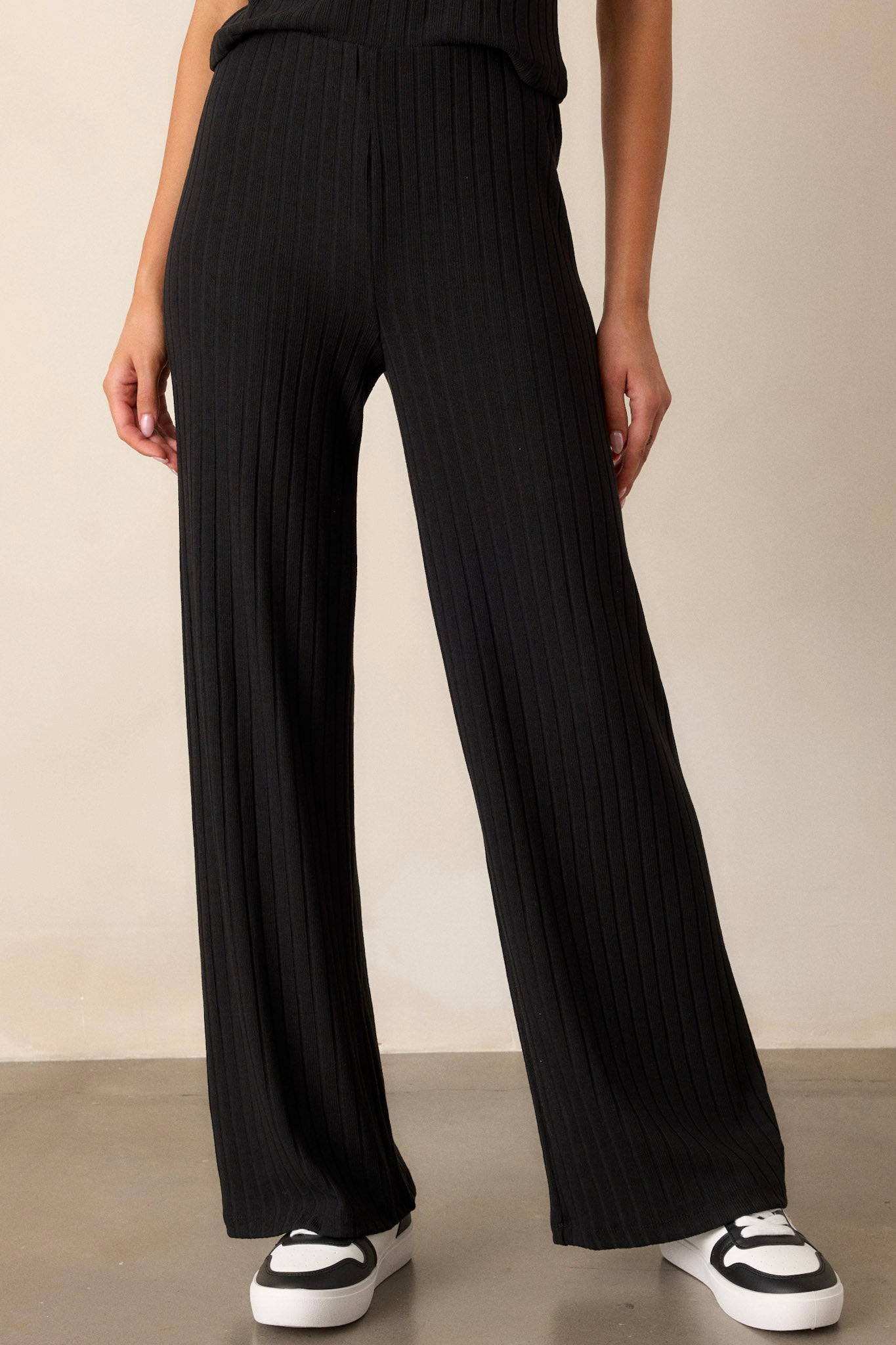 Front view of black pants featuring a high waisted design, a thick elastic waistband, ribbed fabric, and a straight leg cut.