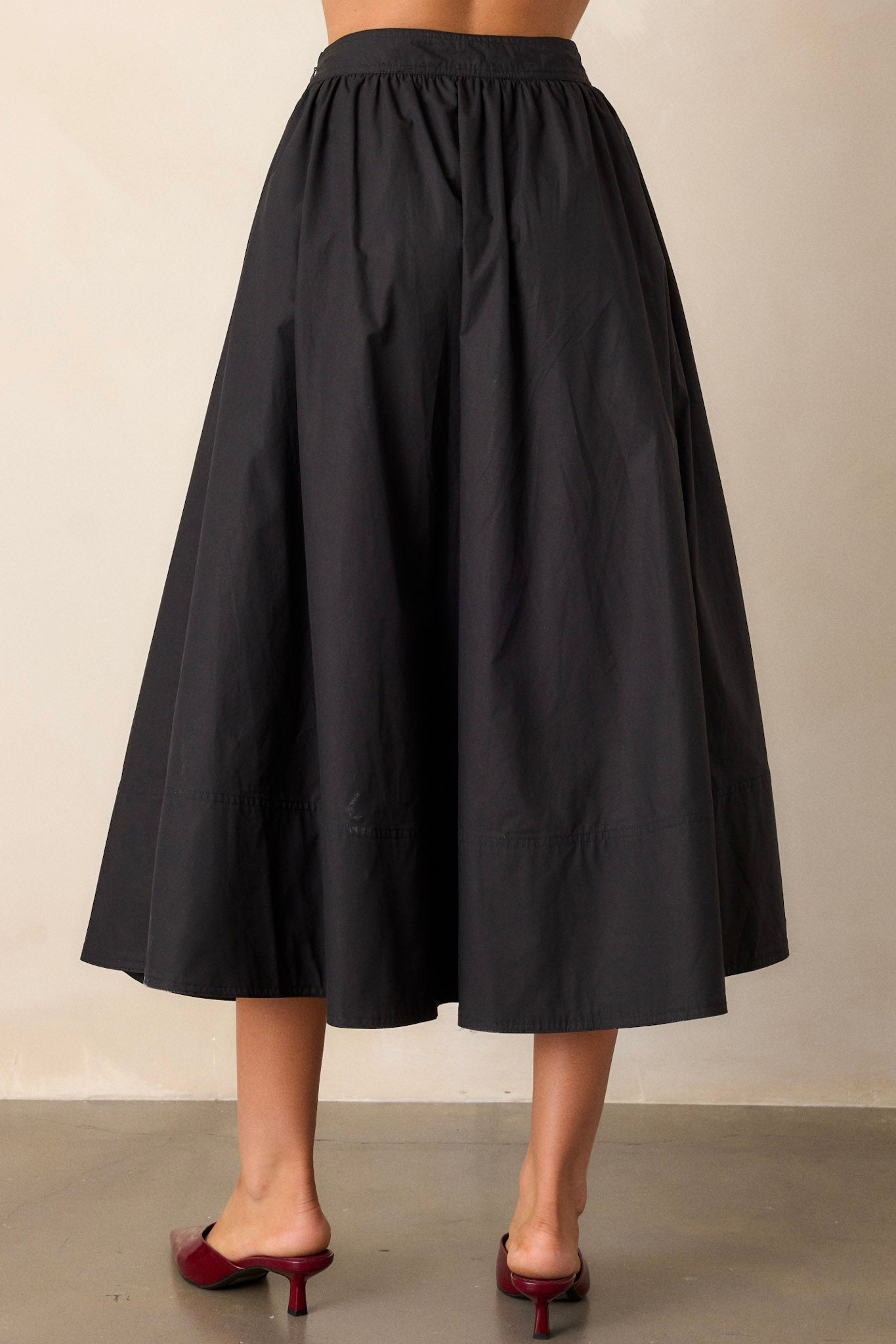 Back view of a black 100% cotton midi skirt highlighting the high waisted design, functional hip pockets, and thick hemline.