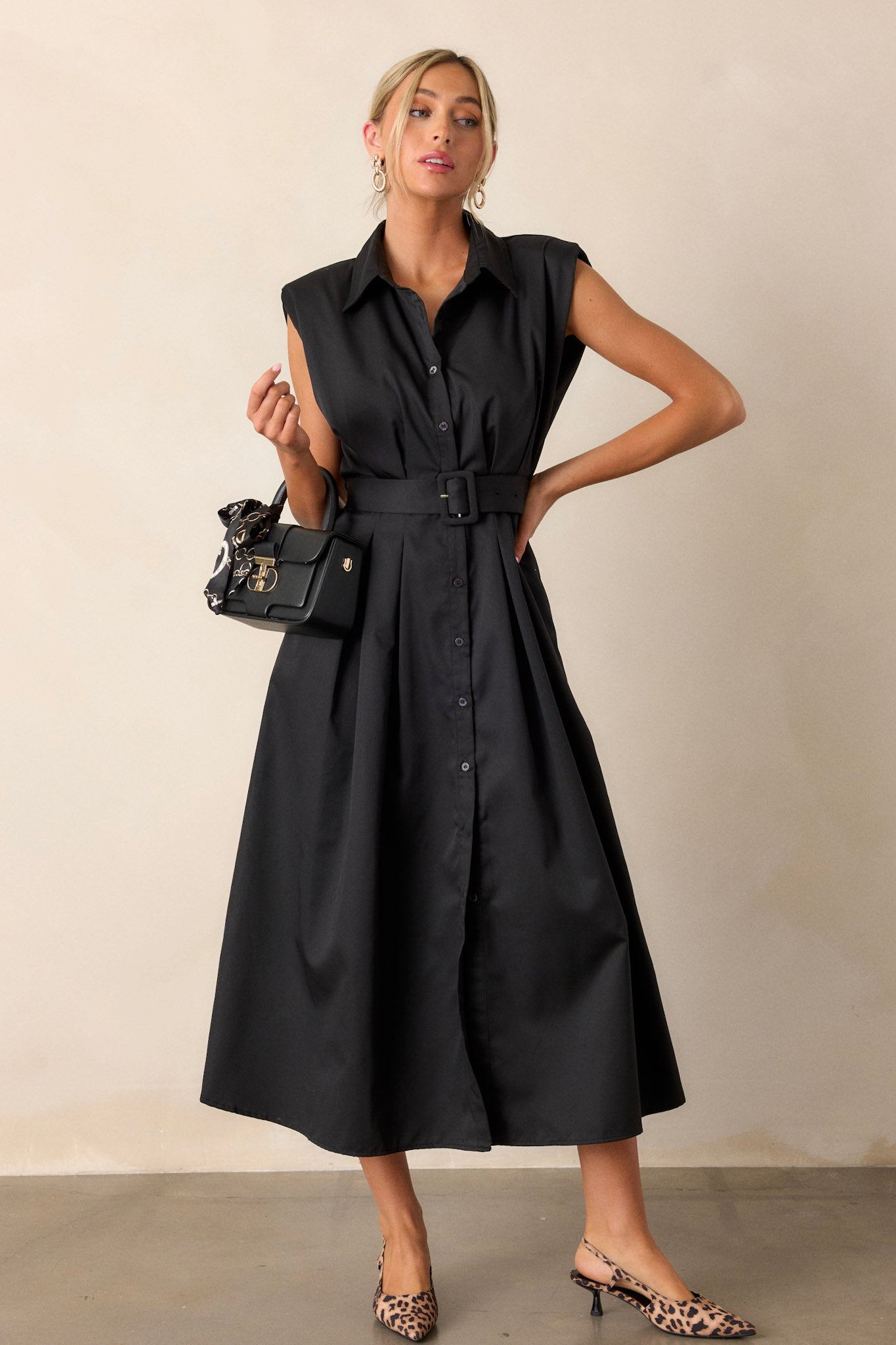 Full body view of this black dress that features built-in shoulder pads, a functional belt and a functional button front.