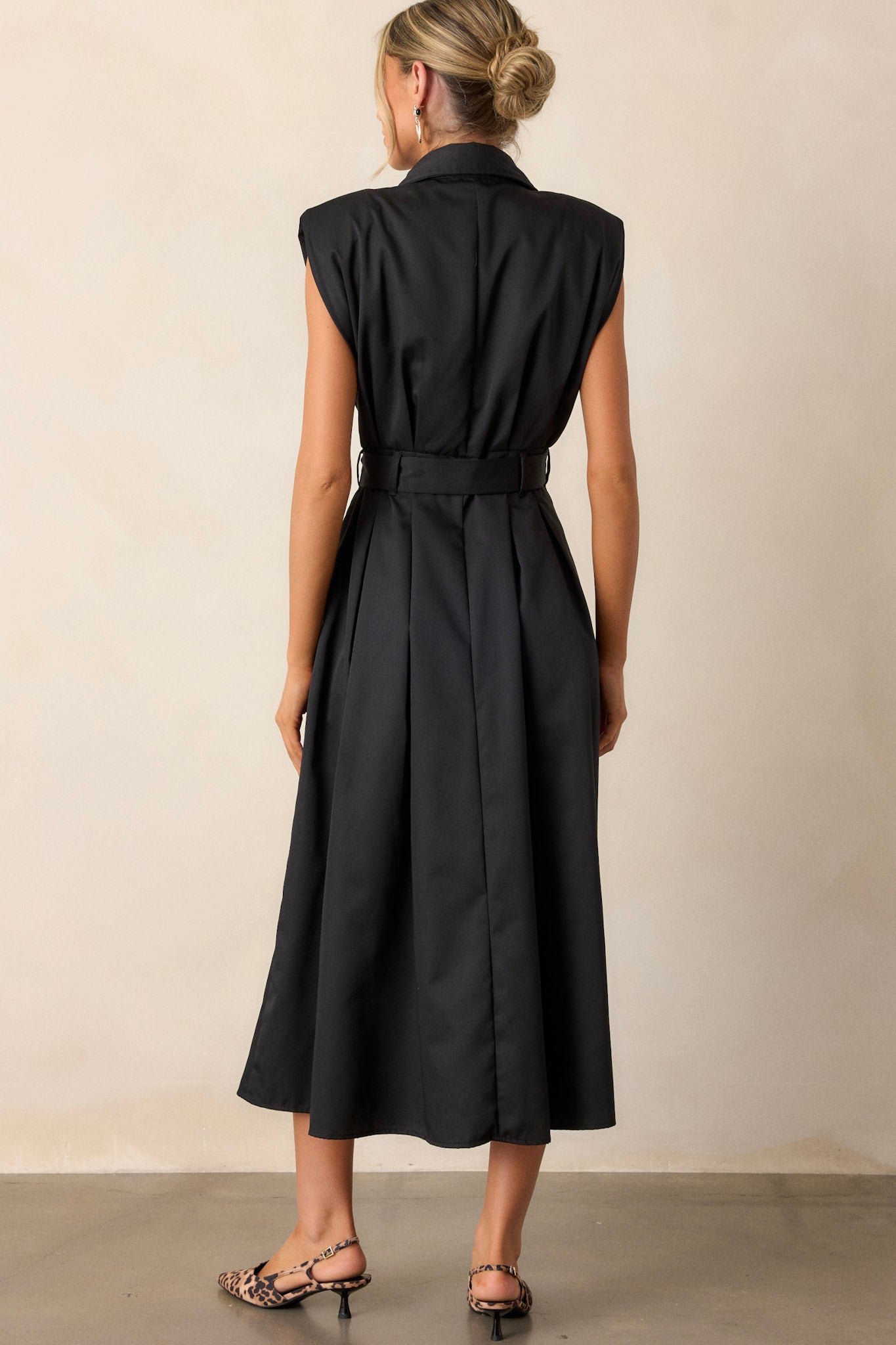 Back view of this black dress that features built-in shoulder pads, a functional belt and a functional button front.