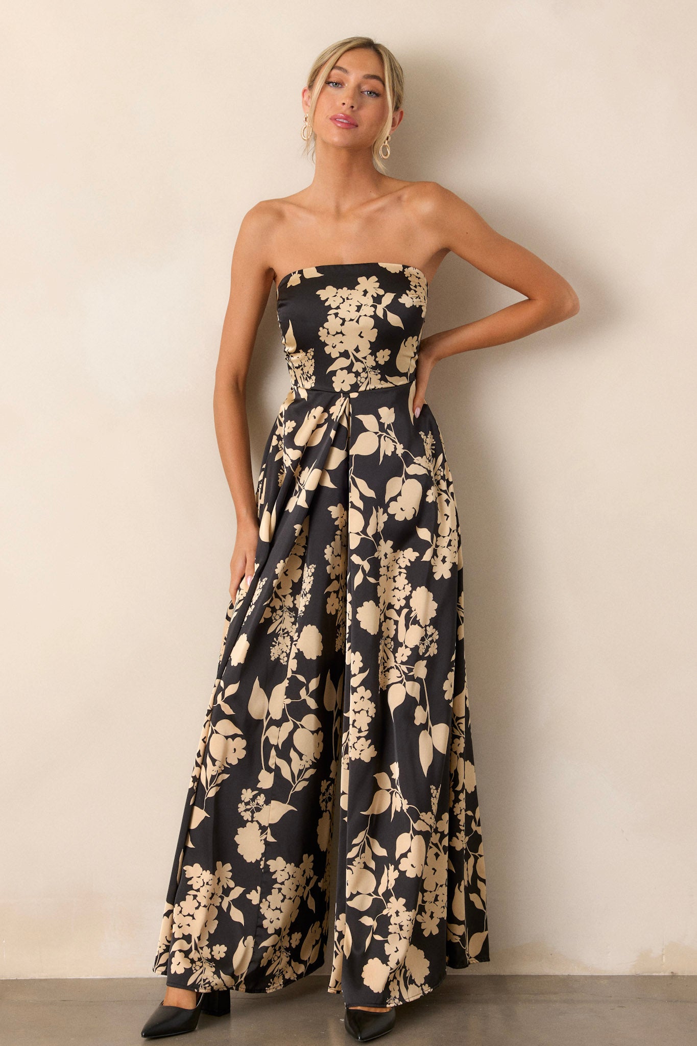 Full length view of the black jumpsuit featuring a bold floral design, a sleeveless cut, and a wide leg silhouette, emphasizing the overall flowy and feminine look.