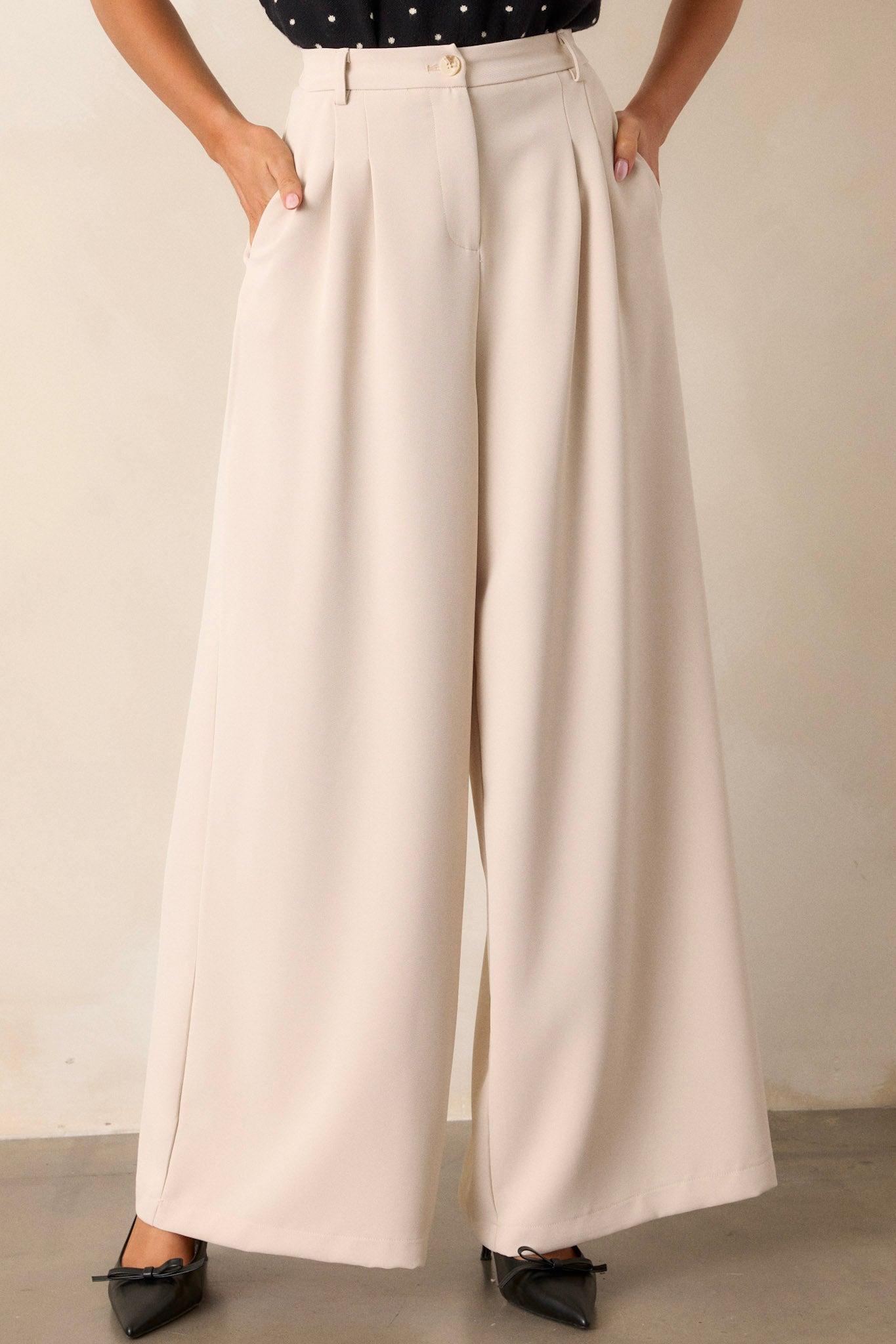 Front angled view of these light taupe pants that feature an elastic waist insert, functional belt loops, a button zipper closure, functional hip pockets, slight pleating on the hips and a wide leg.